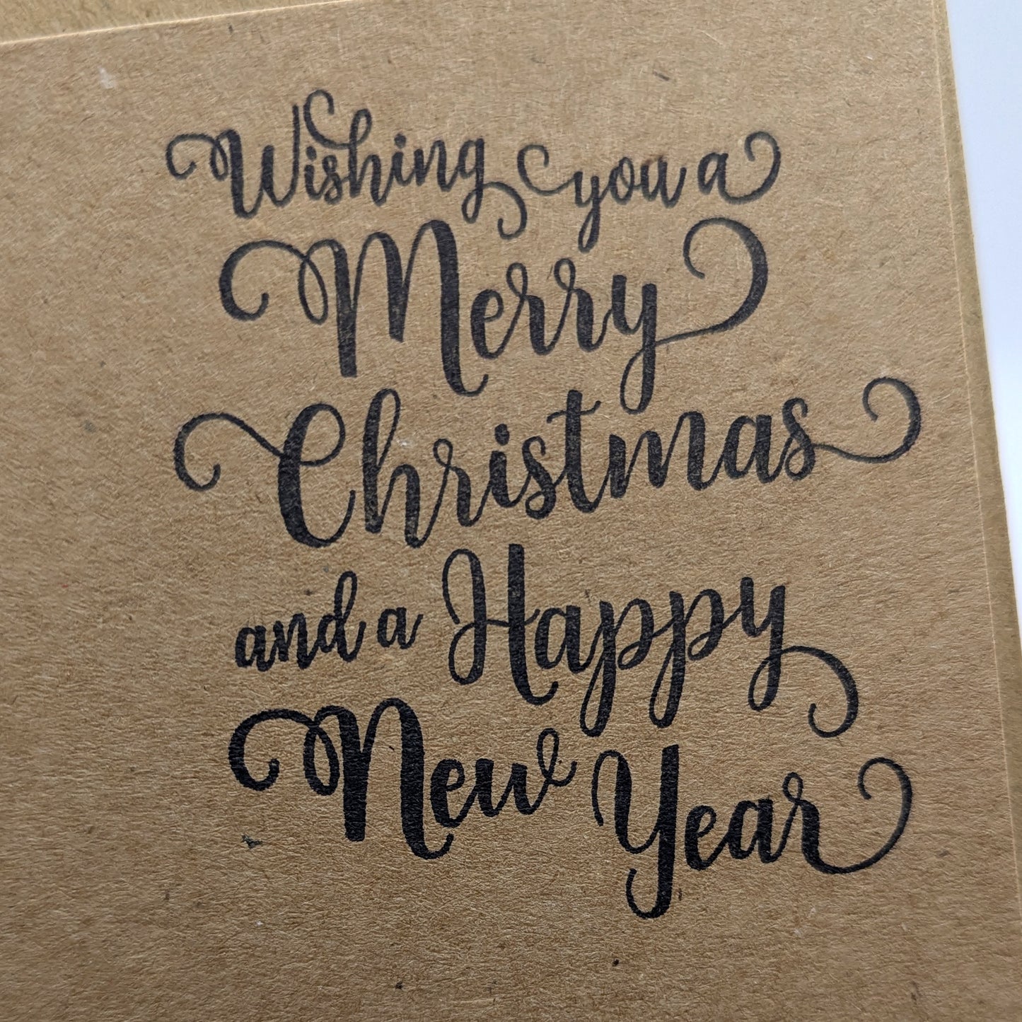 close up of wishing you a merry Christmas and a happy new year, stamped in black ink onto a kraft card