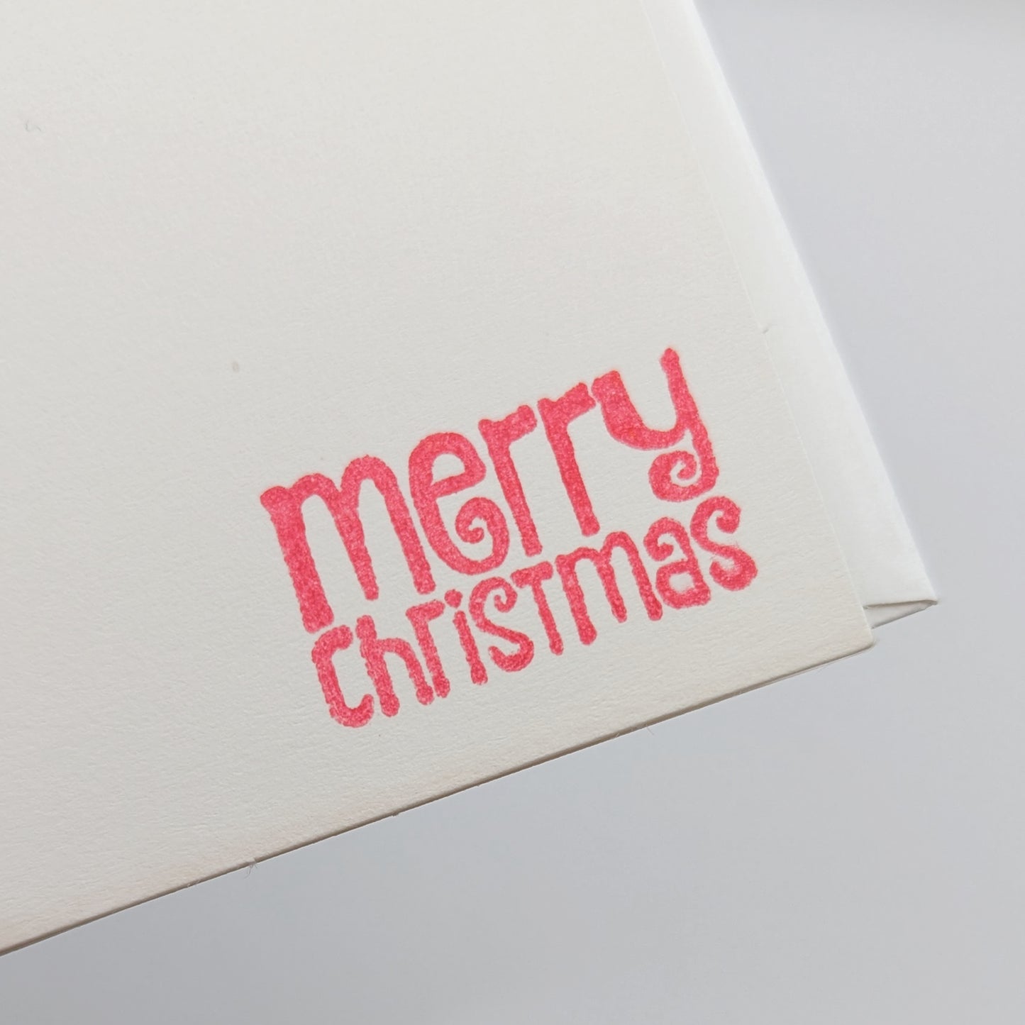 close up of merry Christmas in a modern font, stamped in red ink onto a white card comes with matching envelope
