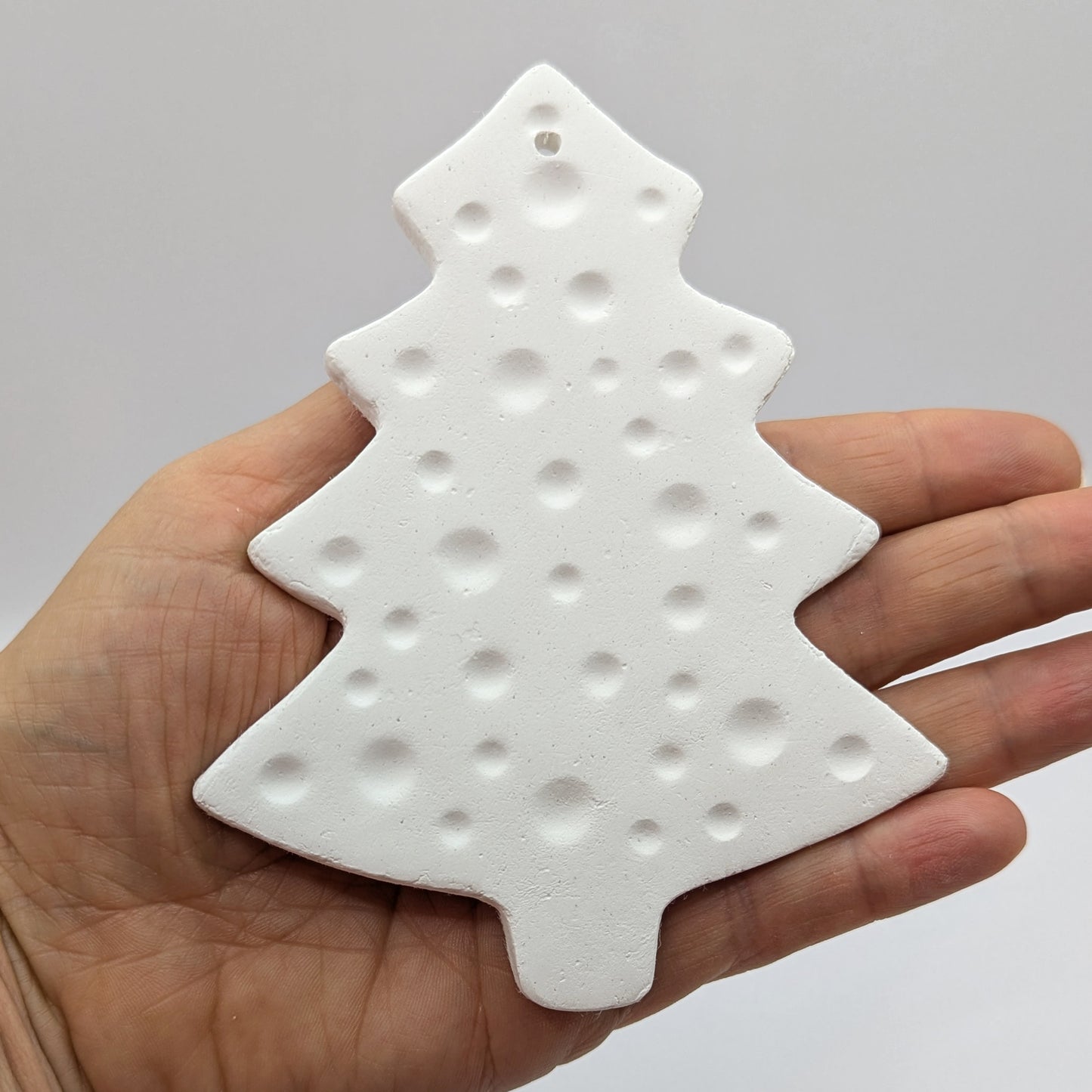 white air dried clay Christmas tree decoration shown in palm of hand with bauble pattern stamped into the clay