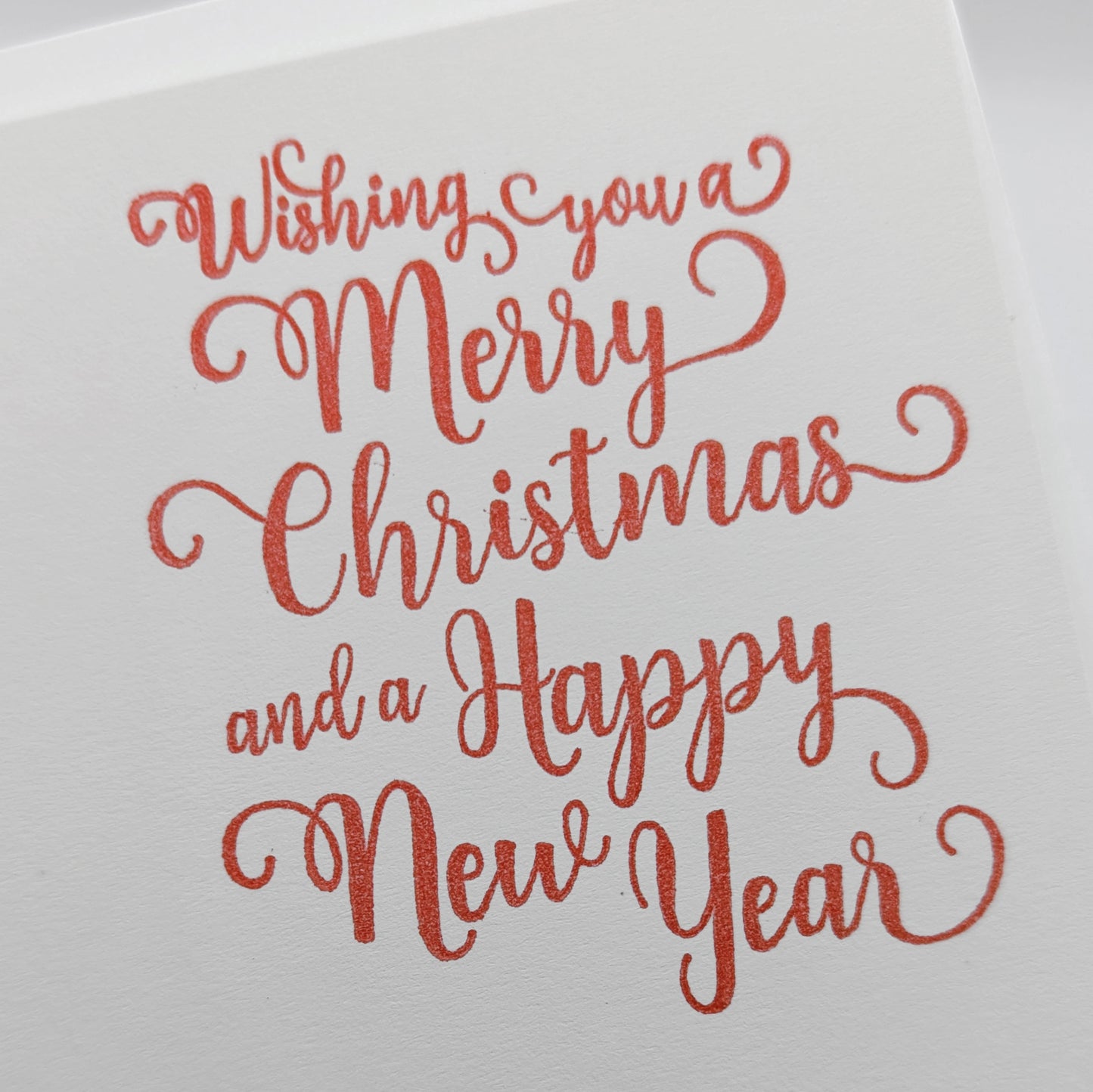 close up of, wishing you a merry Christmas and a happy new year, stamped in red ink onto a white card
