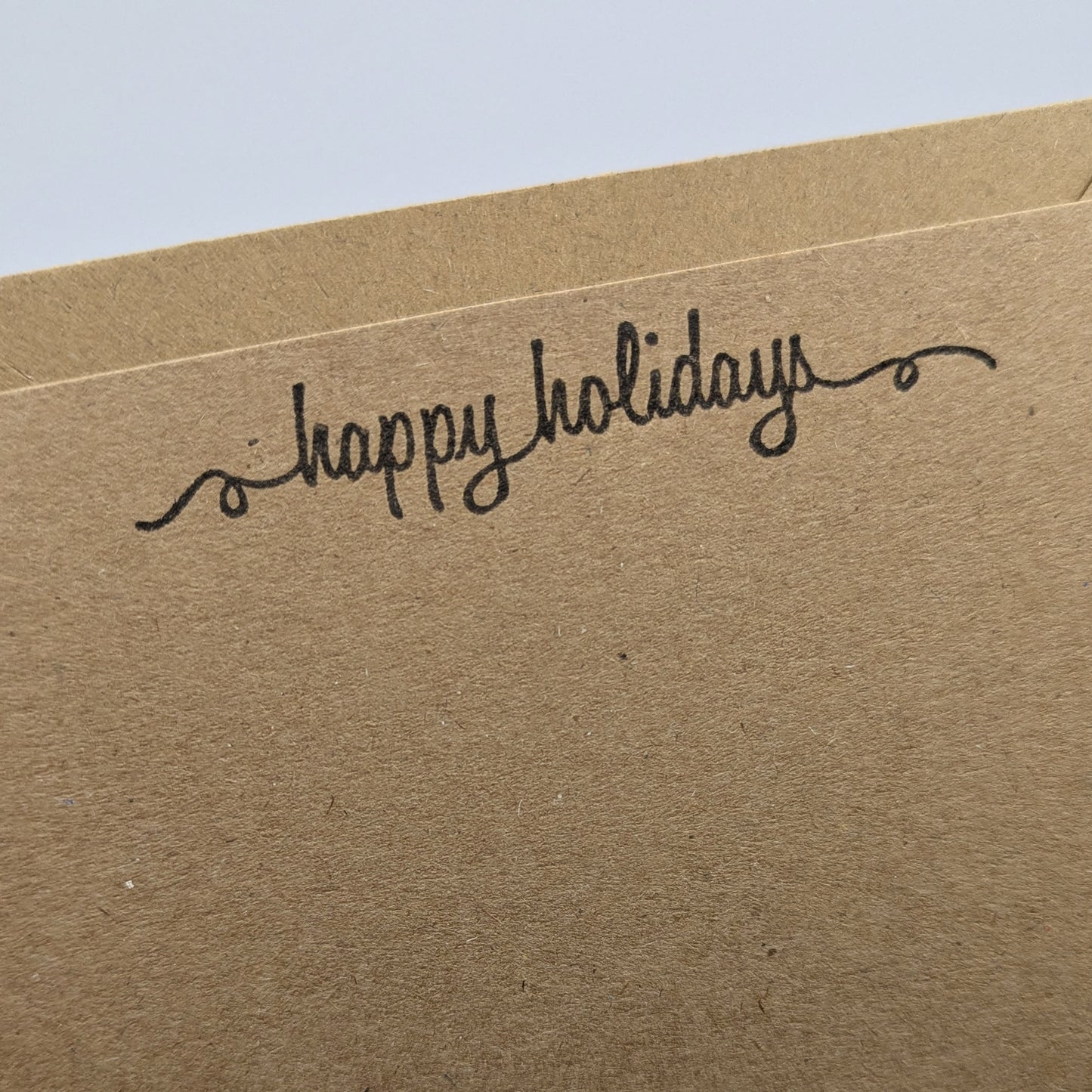 happy holidays stamped in black ink onto a kraft card