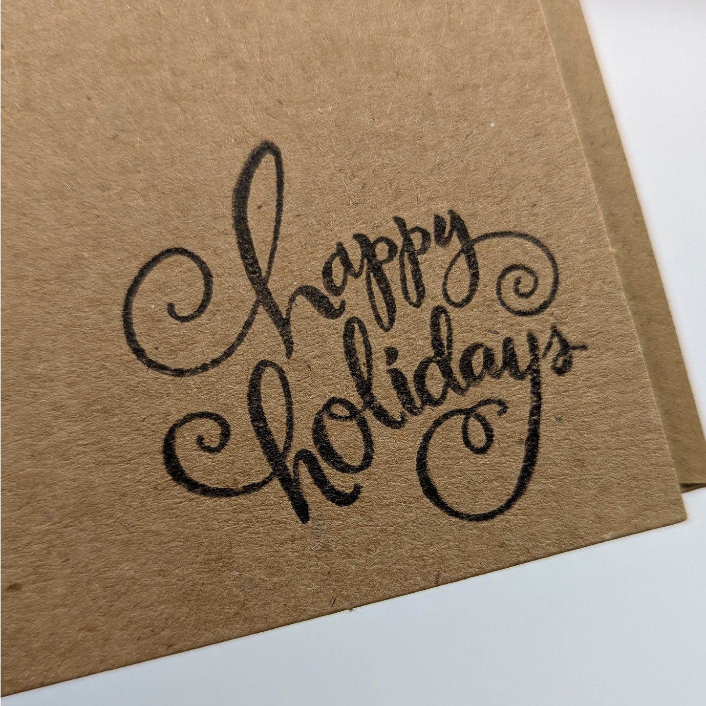 close up of happy holidays stamped in black ink onto a kraft card,