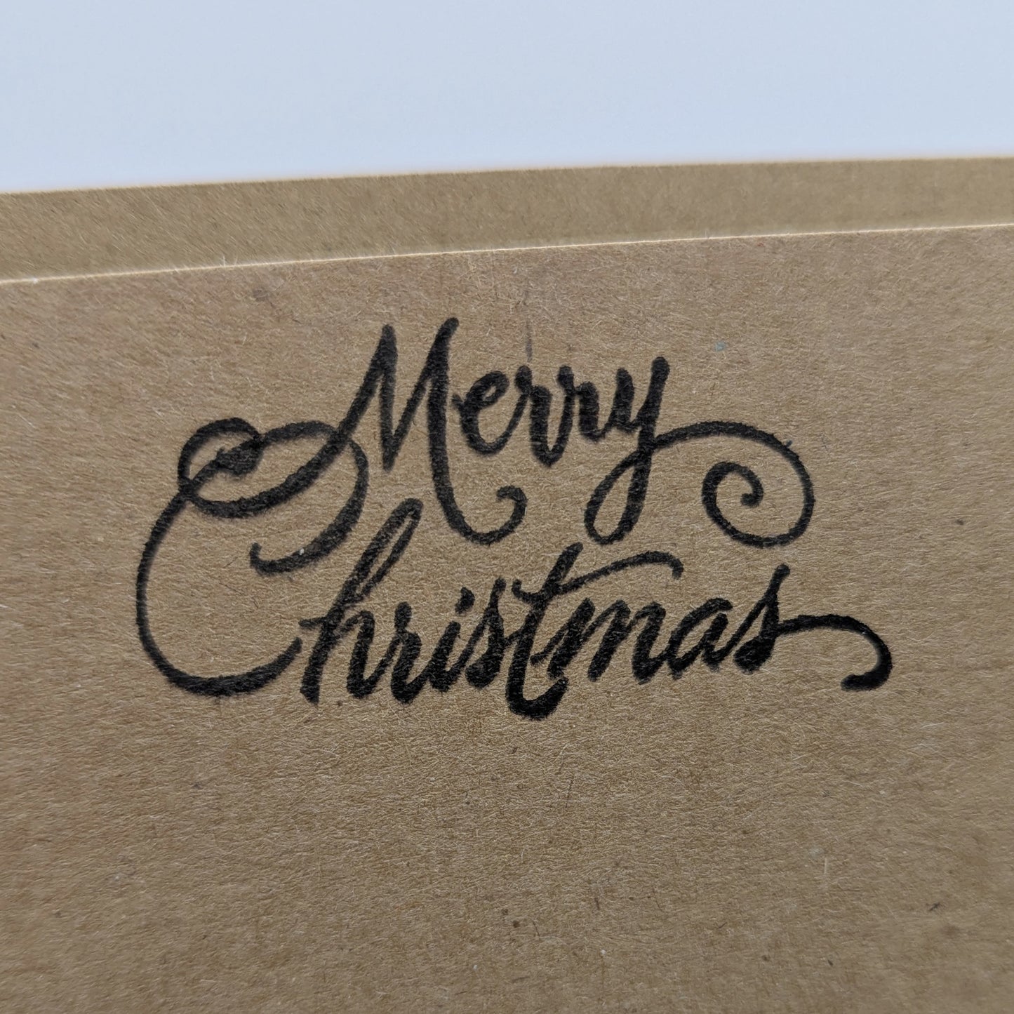 close up of merry Christmas, stamped in black ink onto a kraft card