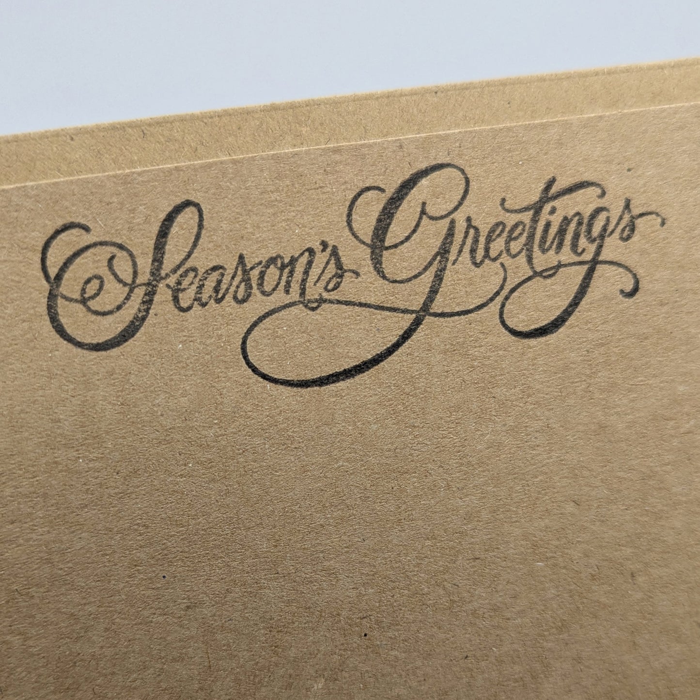 close up of seasons greeting stamped in black ink onto a kraft card