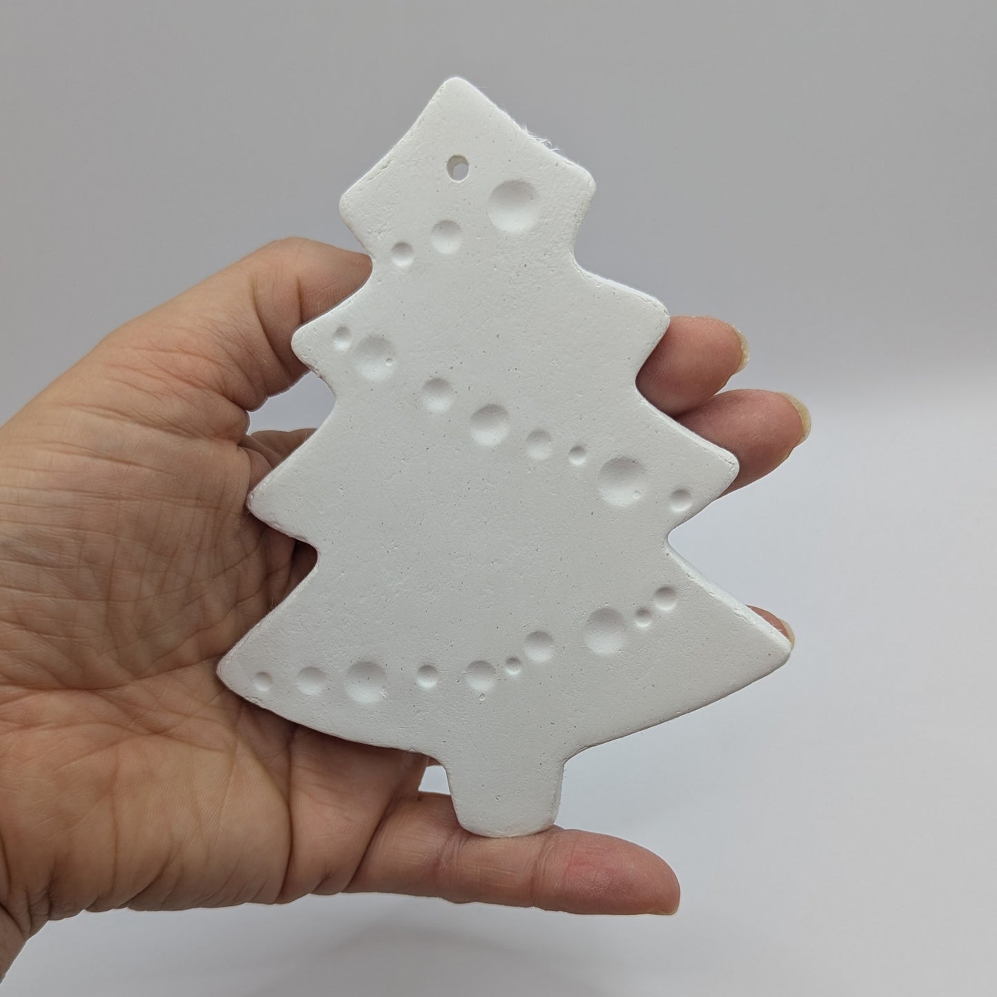 white air dried clay Christmas tree decoration held in hand with tinsel pattern stamped into the clay
