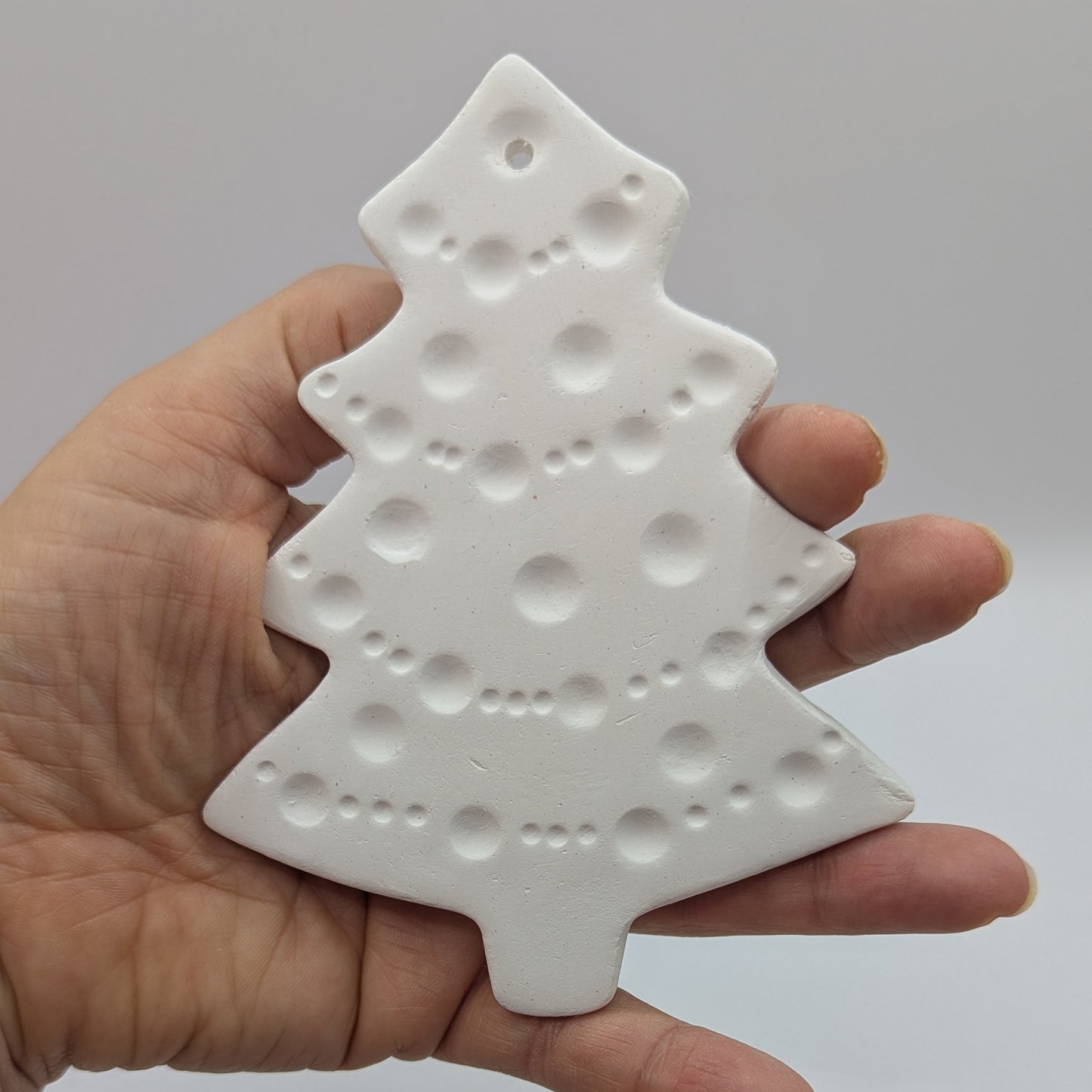 white air dried clay Christmas tree decoration held in hand with tinsel and bauble pattern stamped into the clay