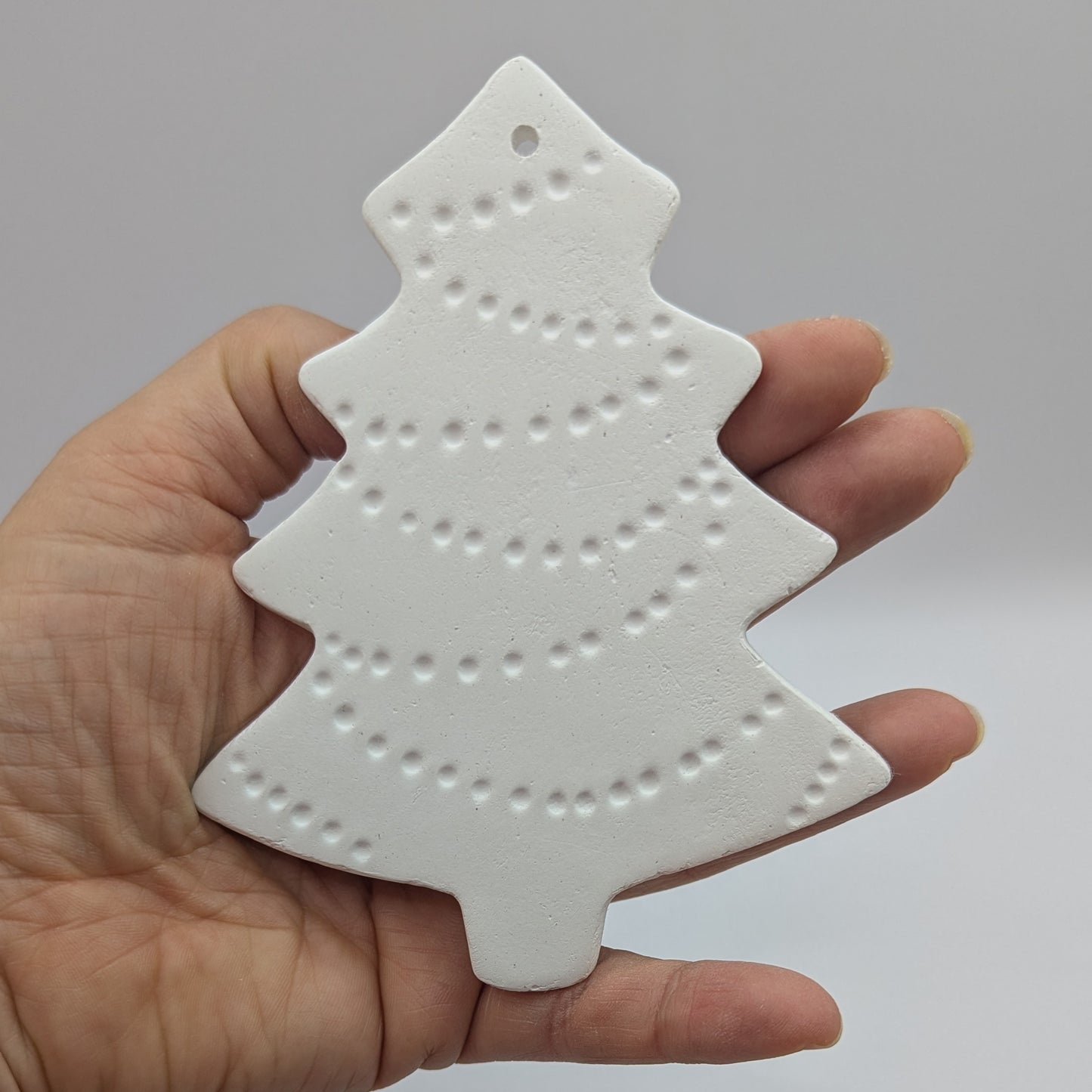 white air dried clay Christmas tree decoration held in hand with tinsel pattern stamped into the clay