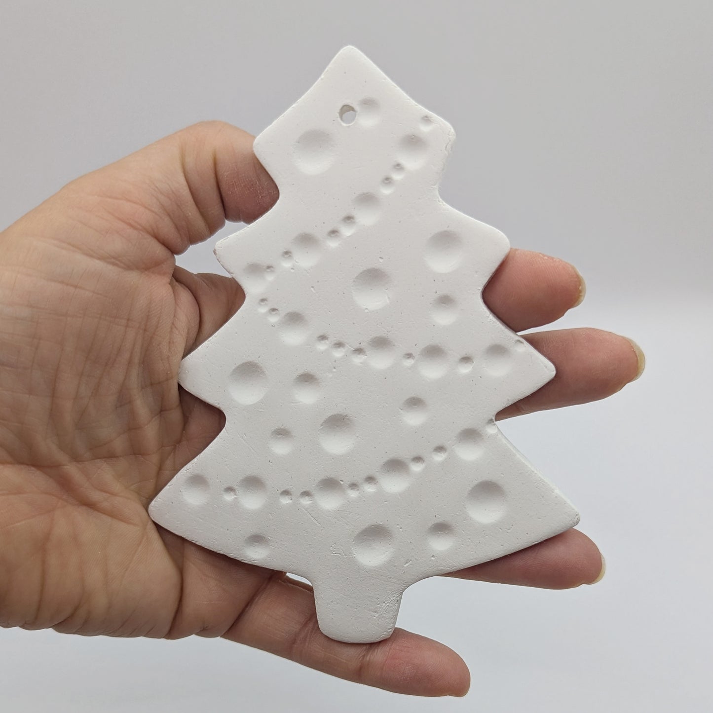 white air dried clay Christmas tree decoration held in hand with tinsel and baubles pattern stamped into the clay
