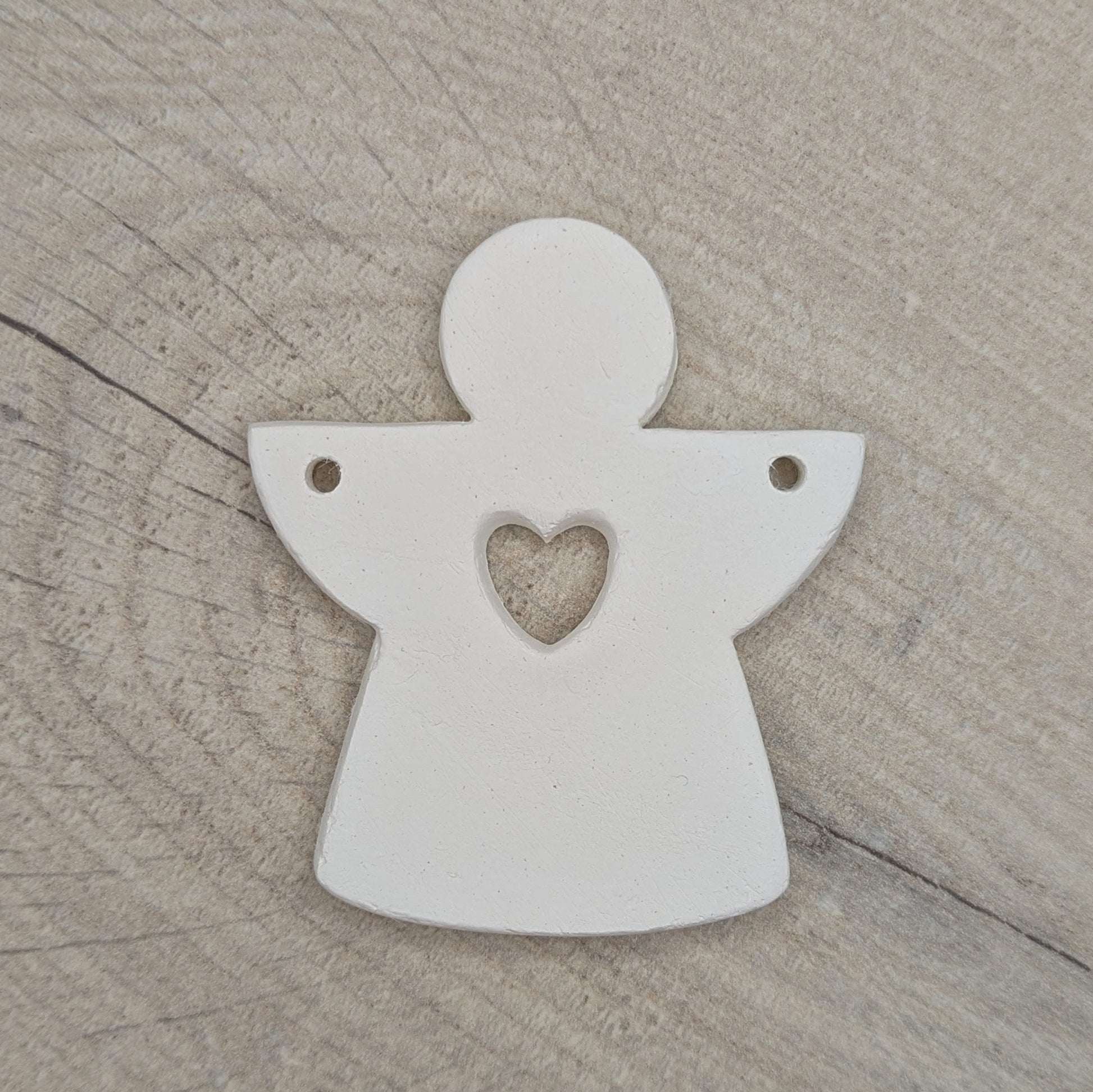 White clay angel ornament with a heart cut out in the heart centre area
