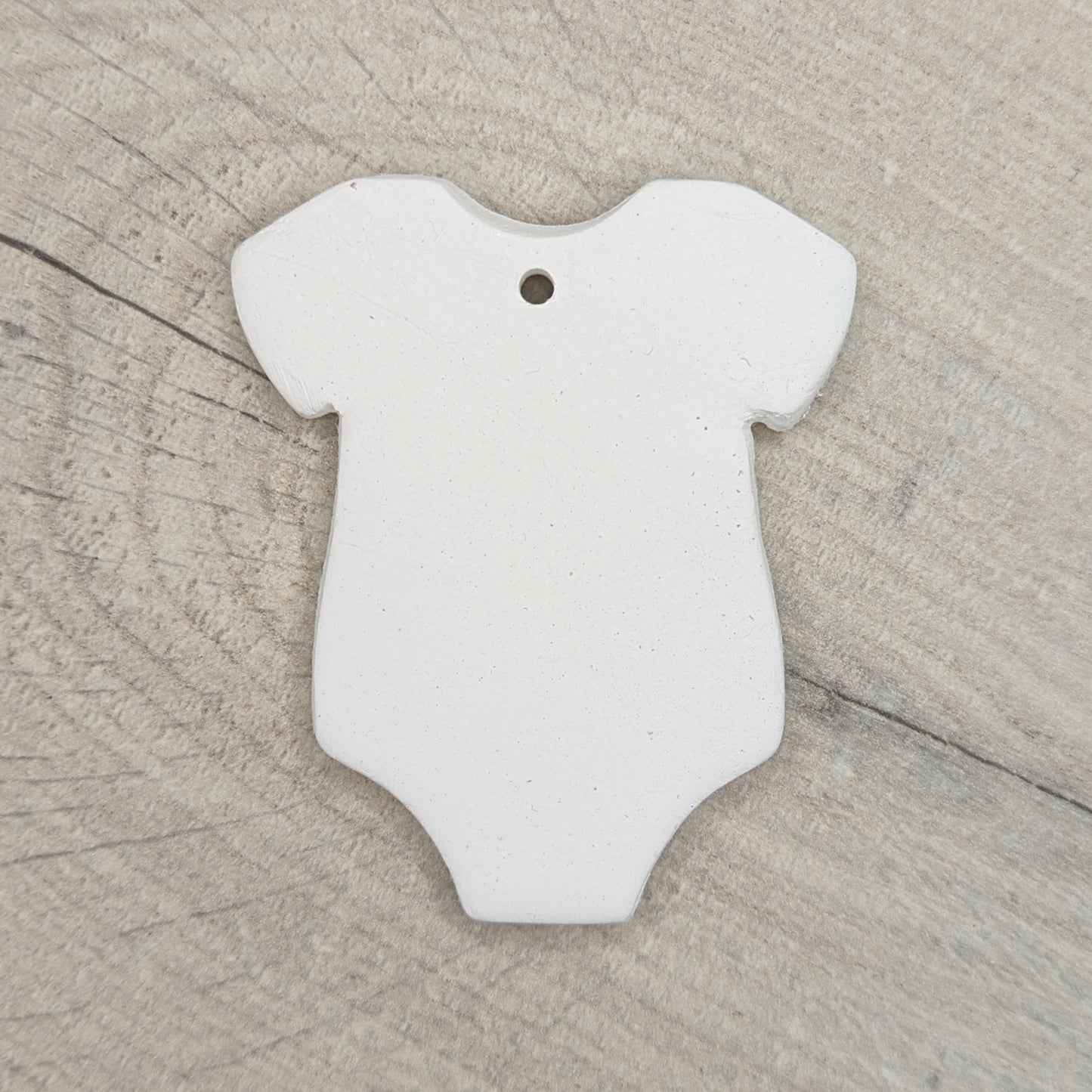 White air dried clay baby onesie / grow on a wooden surface