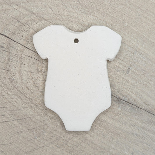 White air dried clay baby onesie / grow on a wooden surface