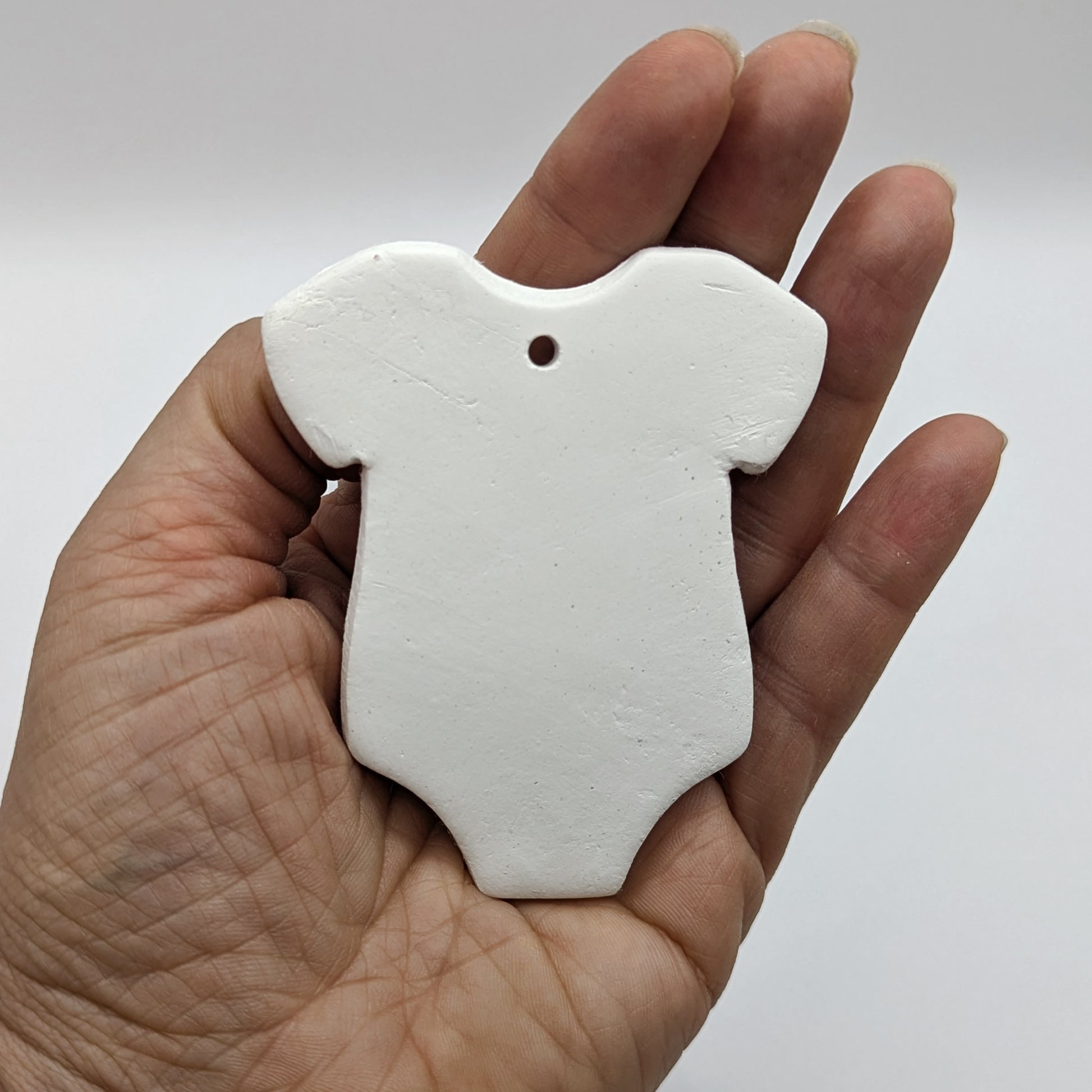 Hand holding a white clay baby grow / onesie