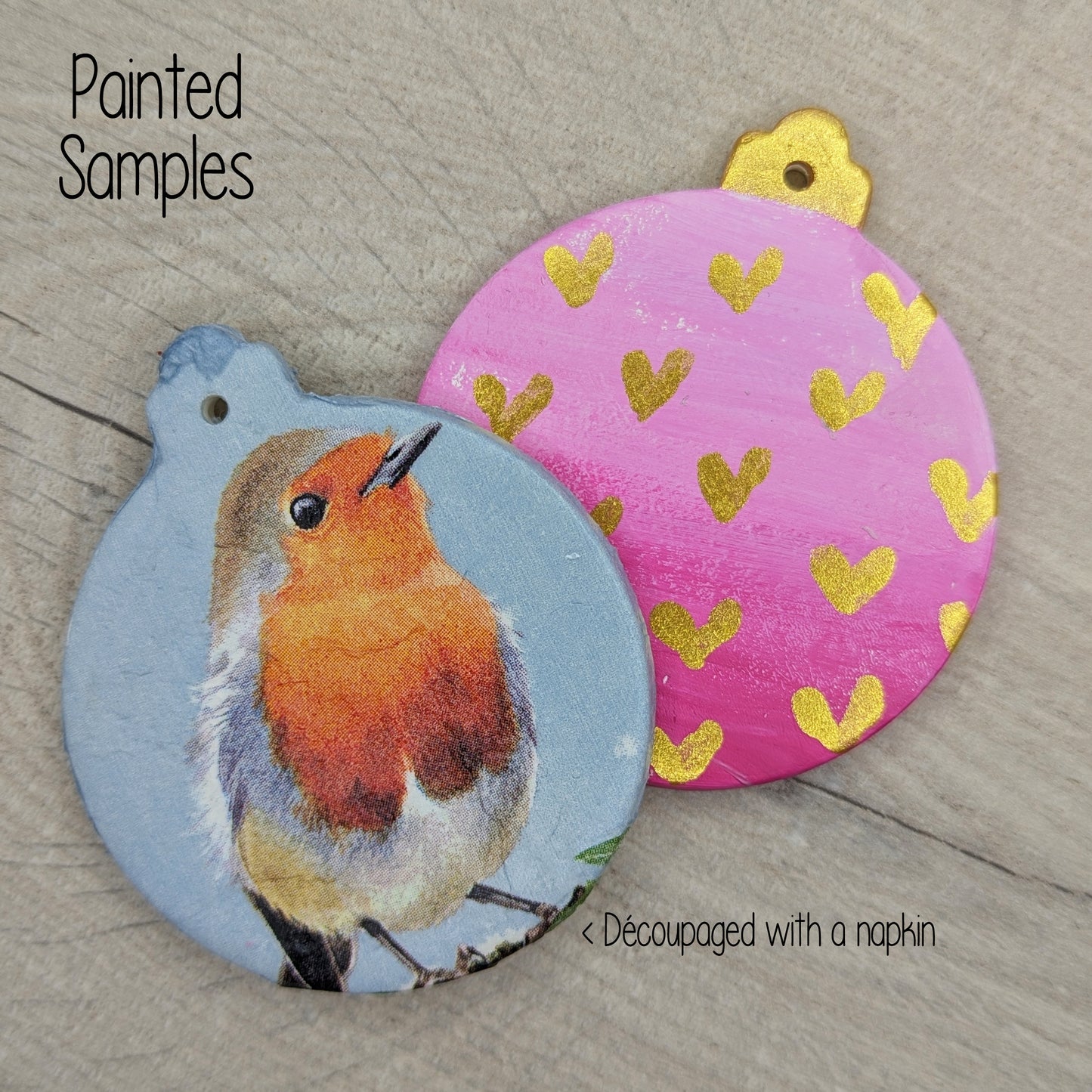 two sample Christmas baubles, one decoupaged with a robin napkin and one painted pastel pink with metallic gold hearts