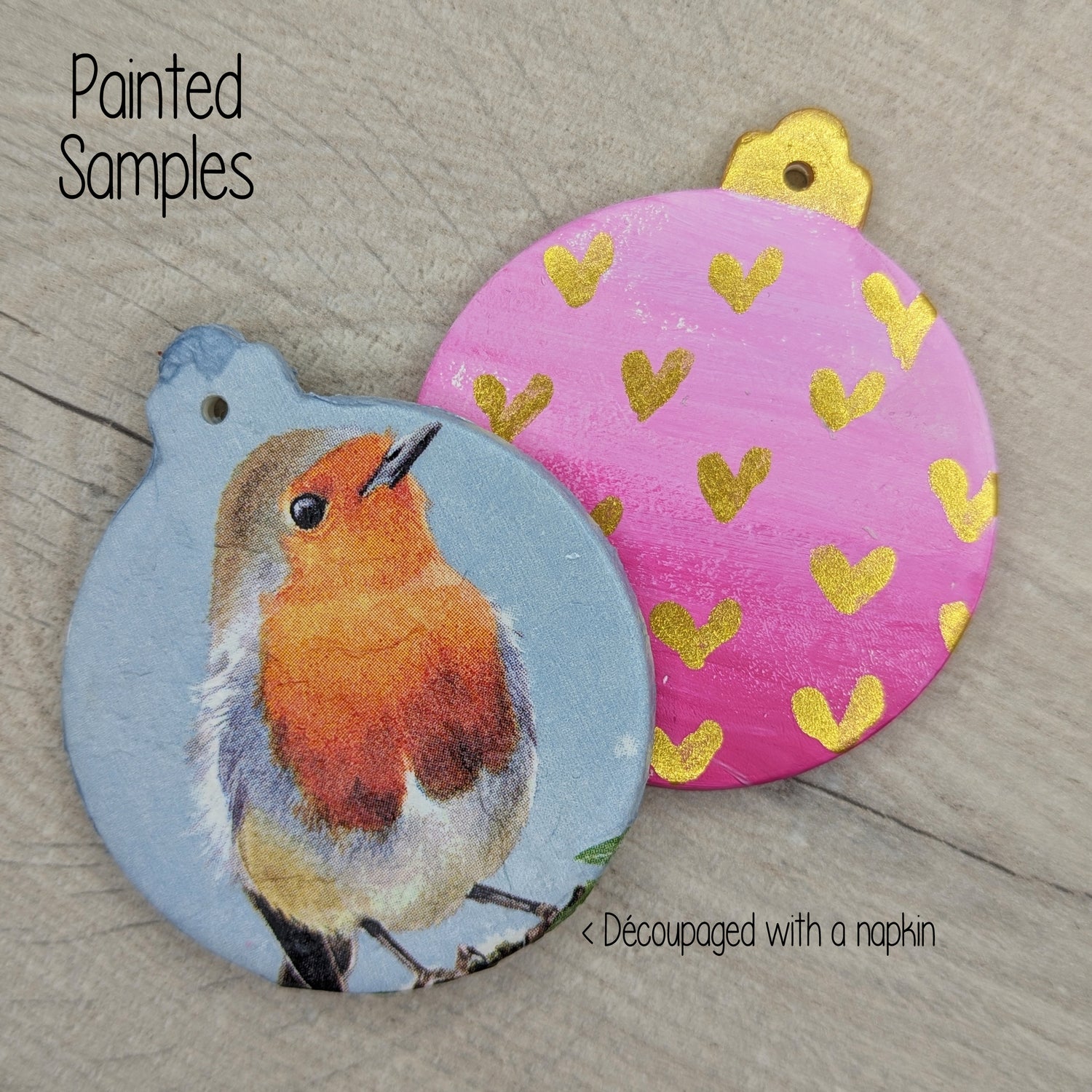 two sample Christmas baubles, one decoupaged with a robin napkin and one painted pastel pink with metallic gold hearts