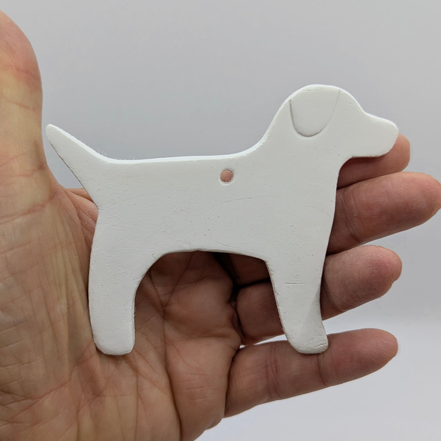 White air dried clay dog-shaped decoration held in some ones hand to show scale