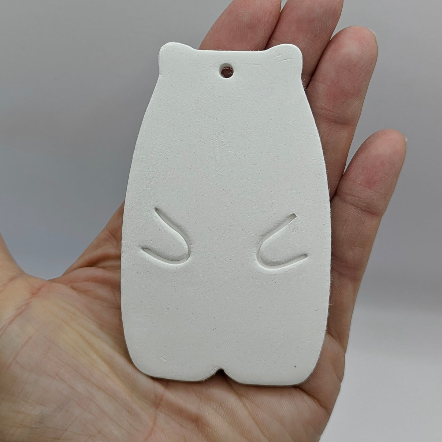 White clay abstract shaped bear on a wooden surface held in a hand against a gray background