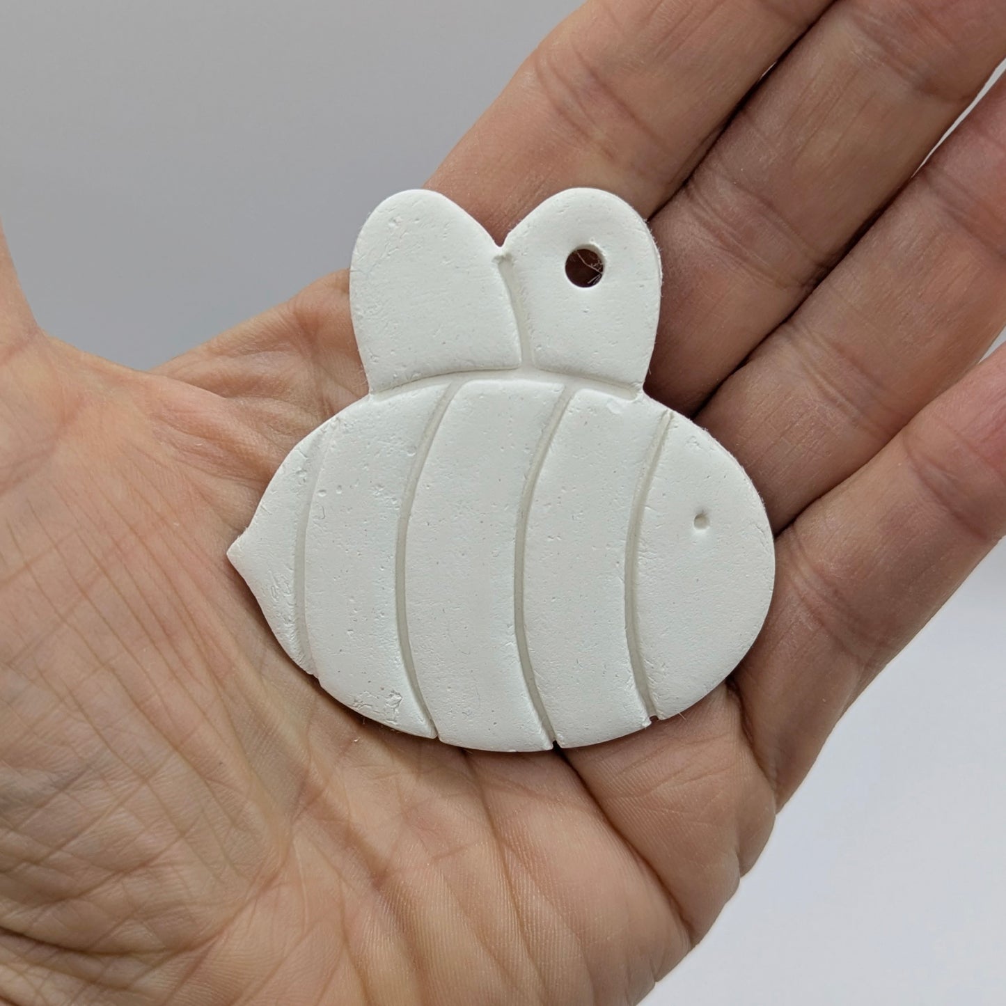 White clay bee held in a hand against a neutral background