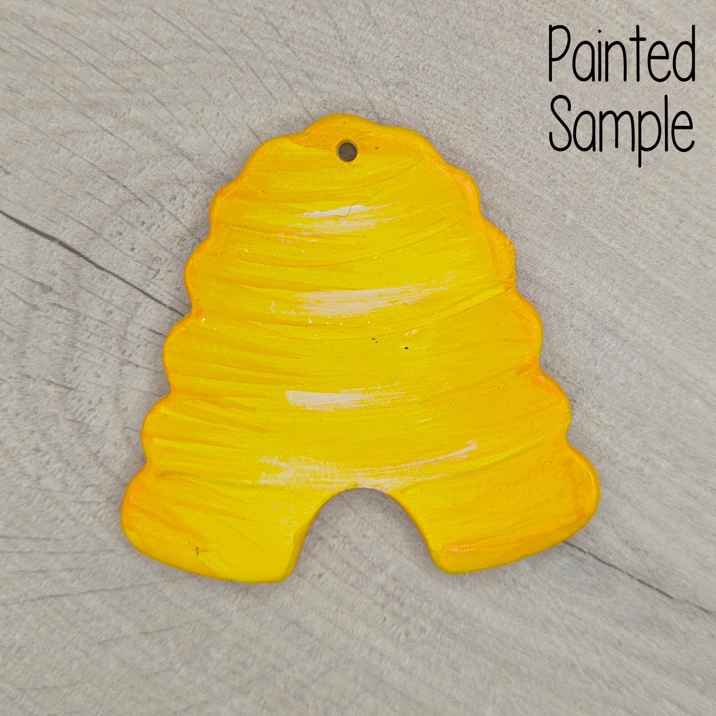 Yellow painted sample beehive clay decoration on a wooden surface with 'Painted Sample' text.