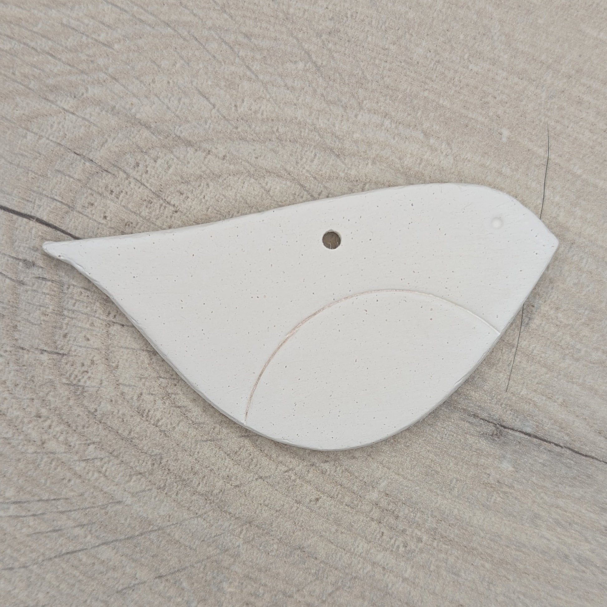 Robin shaped white clay bird  decoration, with chest and eye stamped in, on wooden background