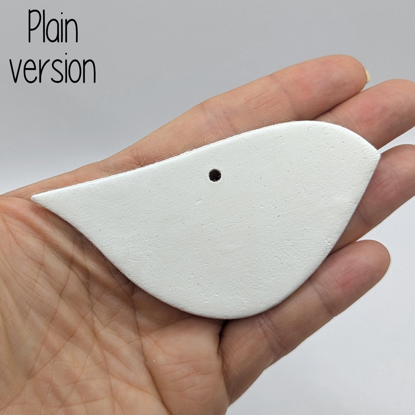 White clay abstract bird shaped clay decoration, held in hand to show scale