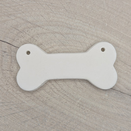 Bone shaped white clay decoration  on a wooden surface, two hanging holes