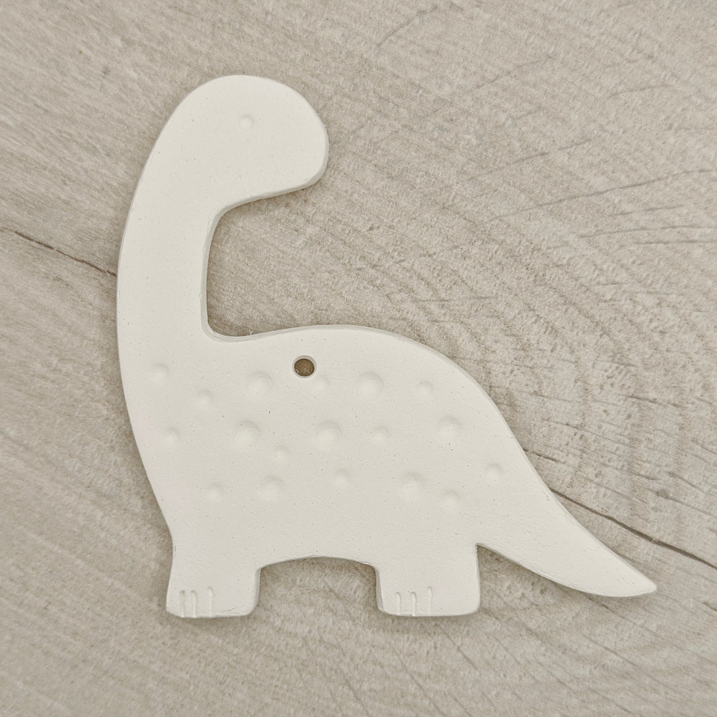 White clay diplodocus dinosaur-shaped decoration on a wooden surface