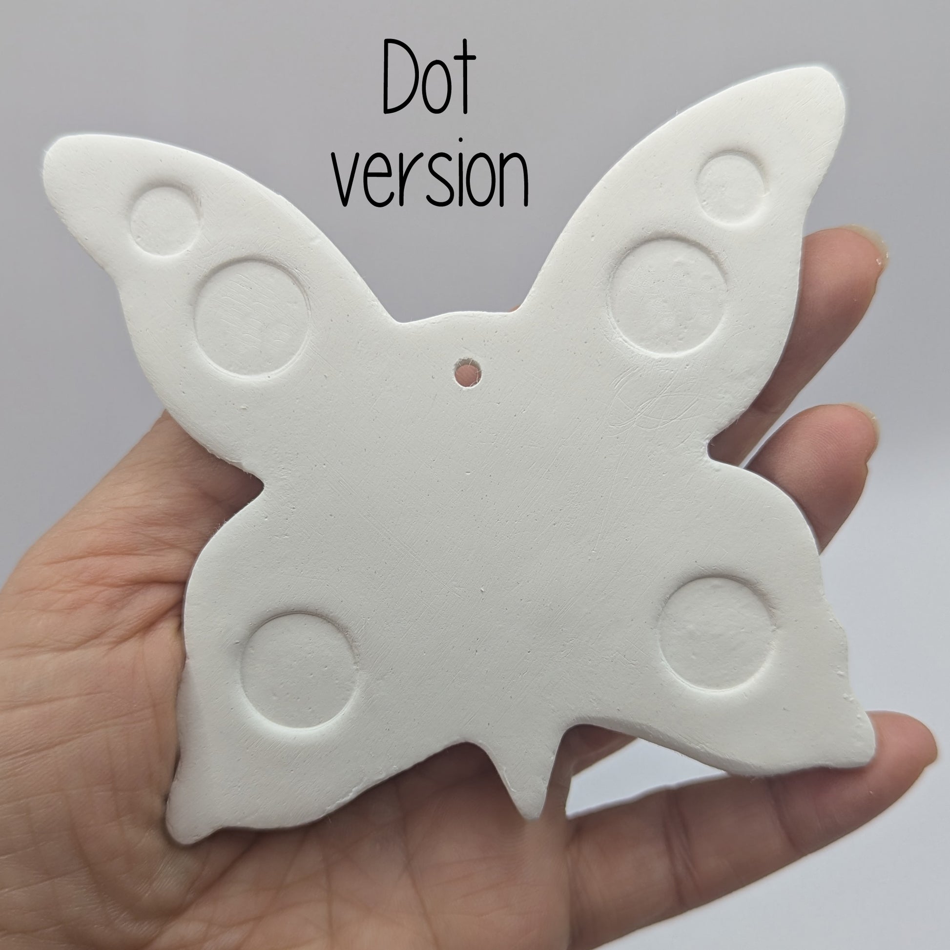 large air dried clay butterfly decoration, with a dotted pattern stamped into the wings, in a ladies hand to show scale