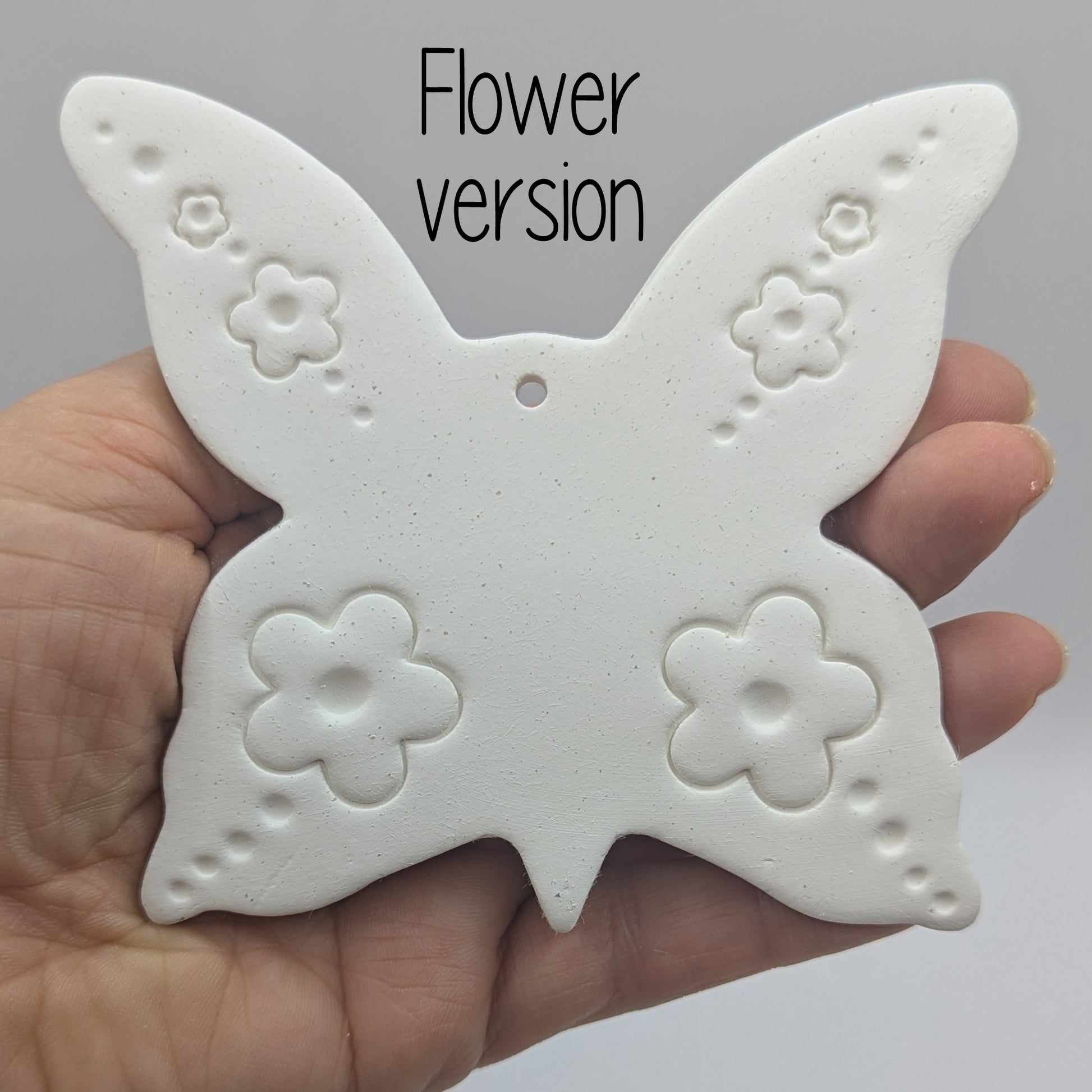 large clay butterfly decoration in a ladies hand to show scale, with a flower pattern stamped into the wings
