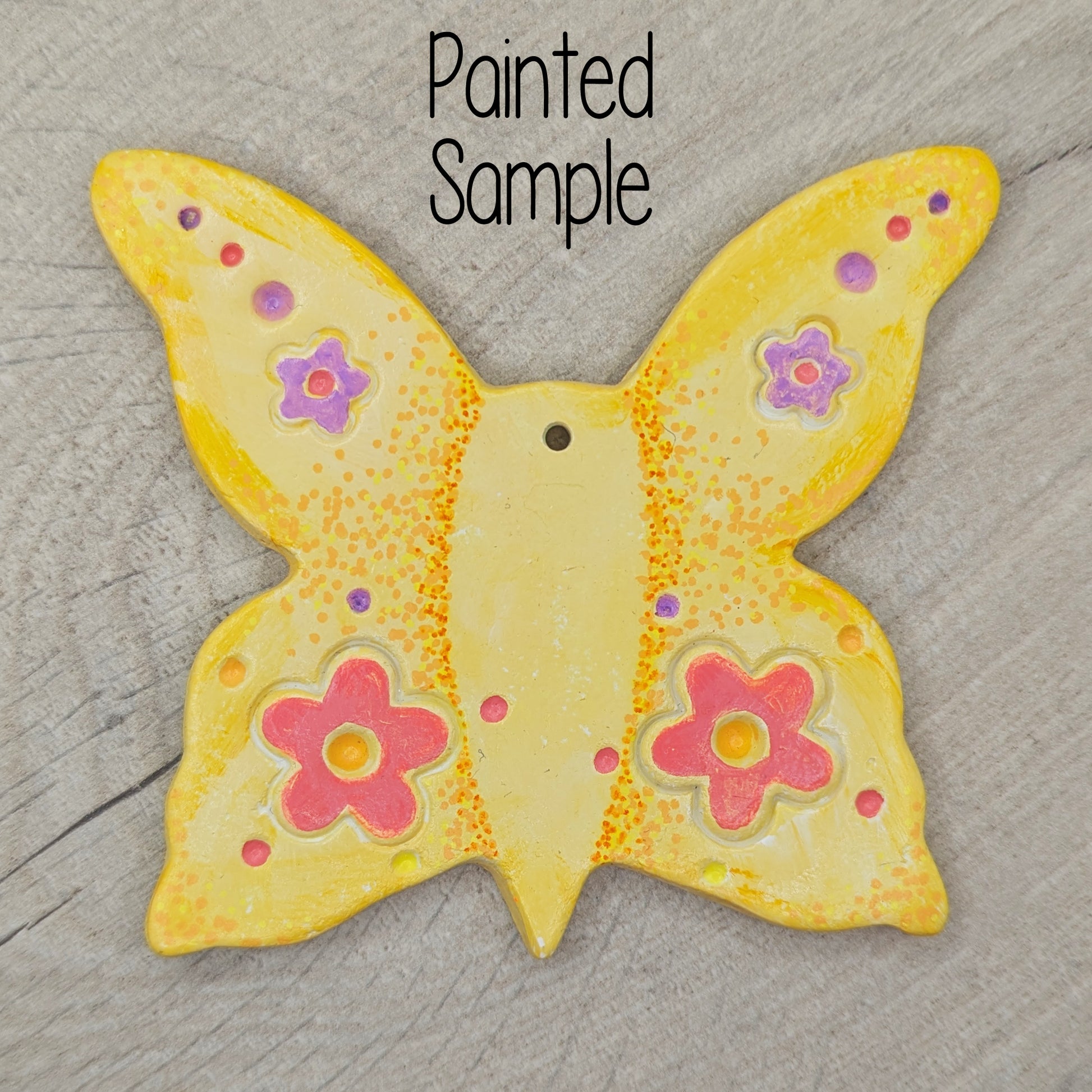sample of large clay butterfly decoration, painted in pastel yellow with pink and lilac flowers on the wings