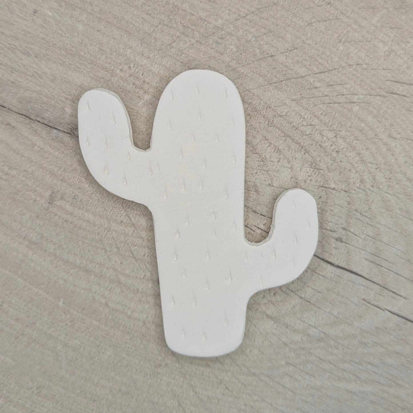 cactus shaped clay decoration, with spike details stamped in on a light wooden background