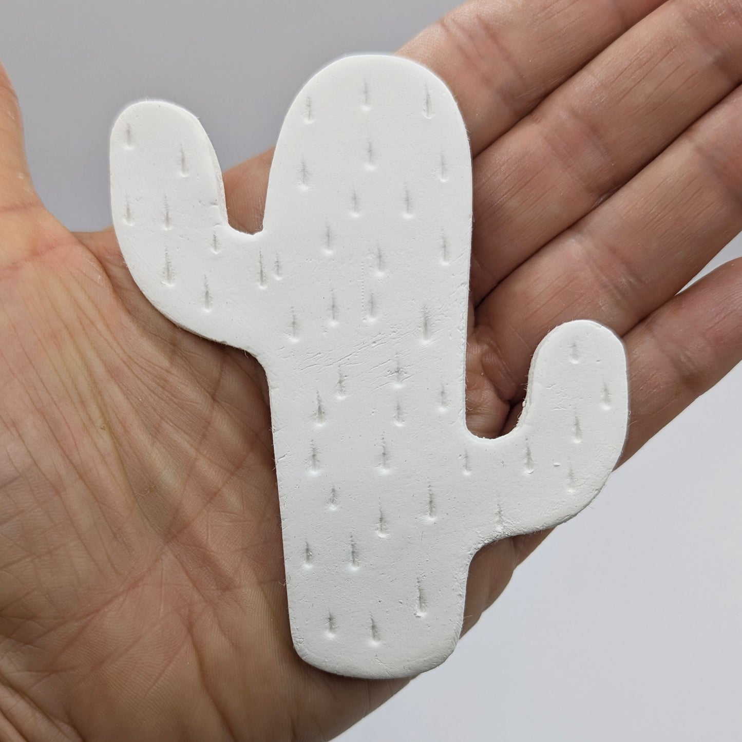 cactus shaped clay decoration, with spike details stamped in, held in a palm to show scale