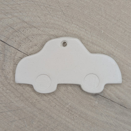White clay car shaped object, with car wheels stamped into the clay on a wooden surface