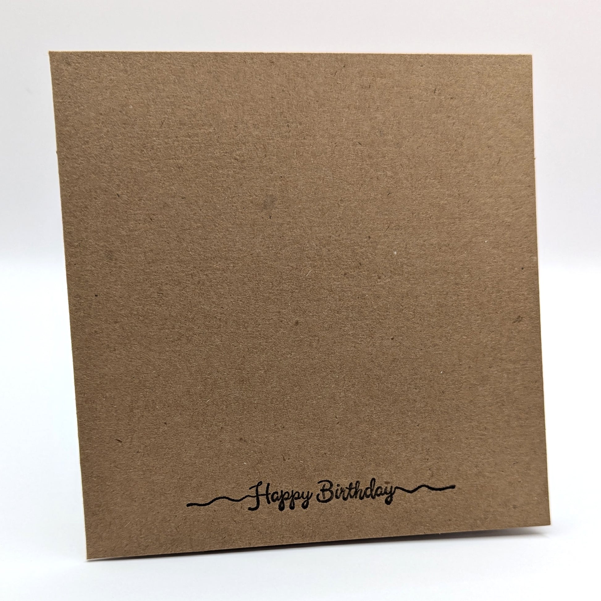 happy birthday stamped in black ink onto the bottom edge of a kraft card