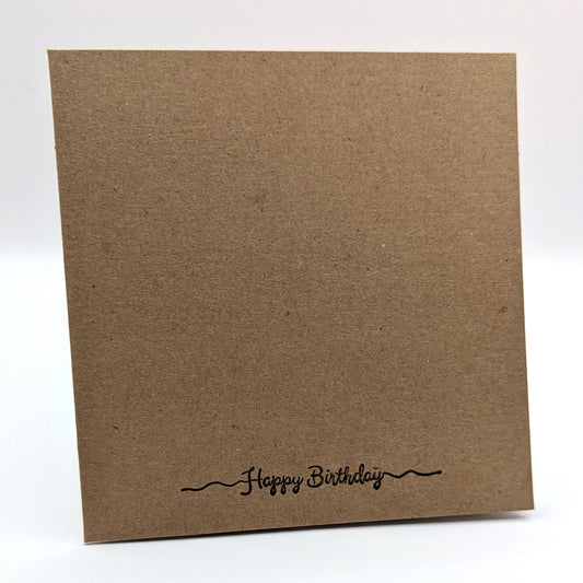 happy birthday stamped in black ink onto the bottom edge of a kraft card