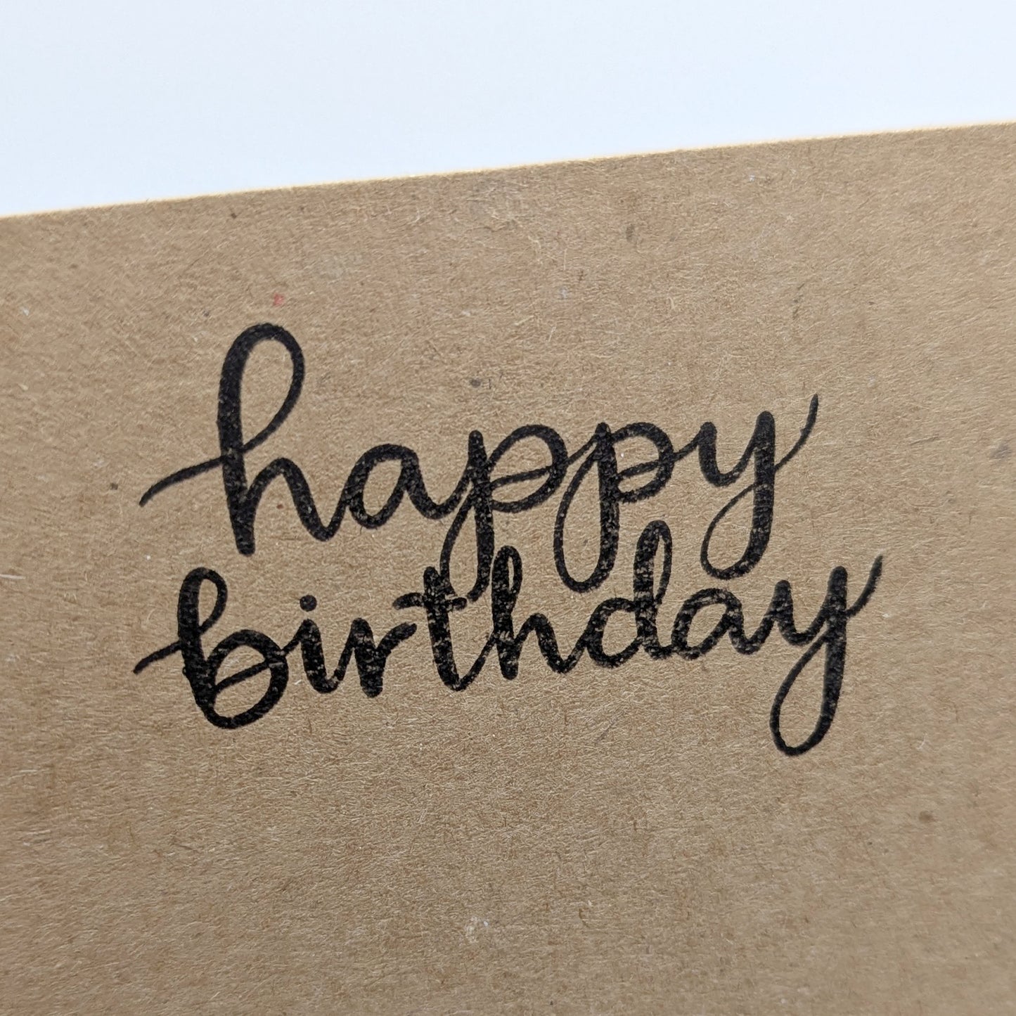 happy birthday in script font stamped in black ink onto a kraft card
