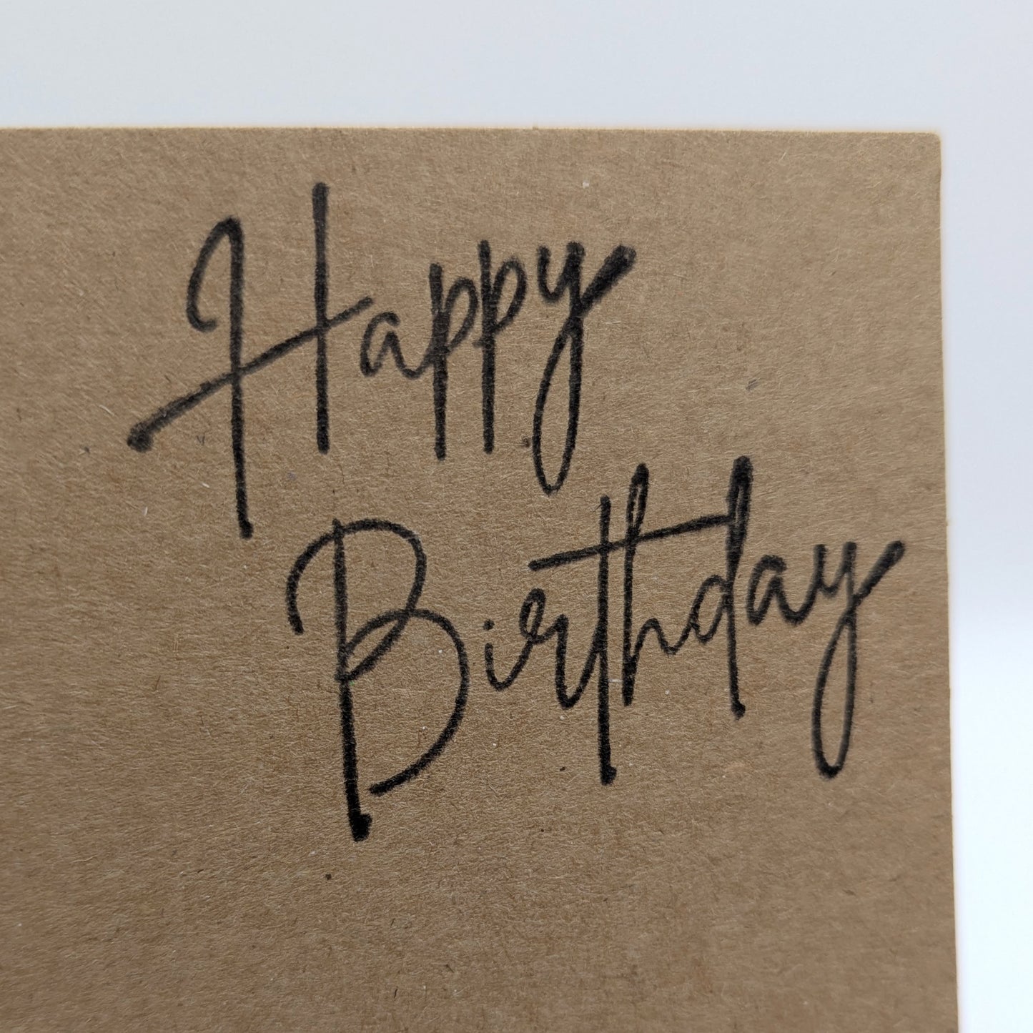 happy birthday stamped onto the corner of a kraft card in black ink