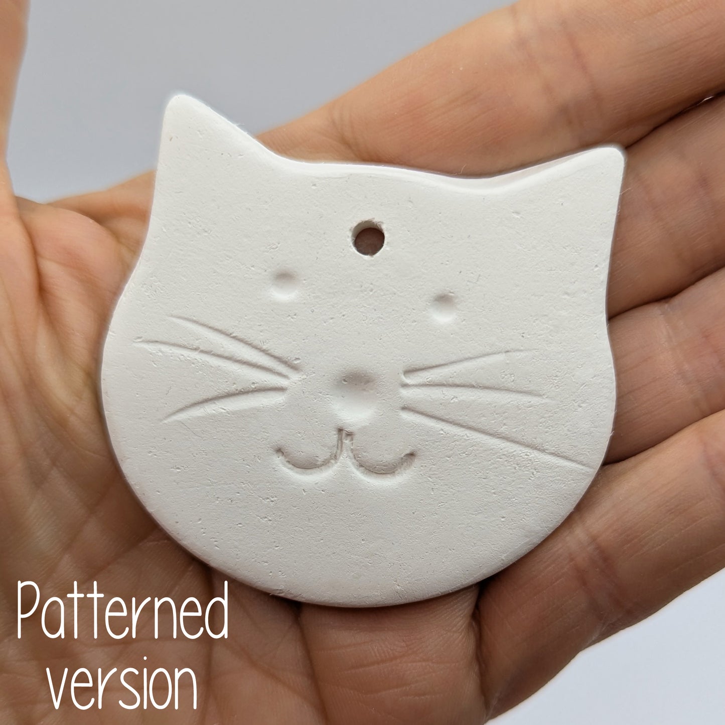 small cute cat face clay decoration being held in the palm of someones hand to show size