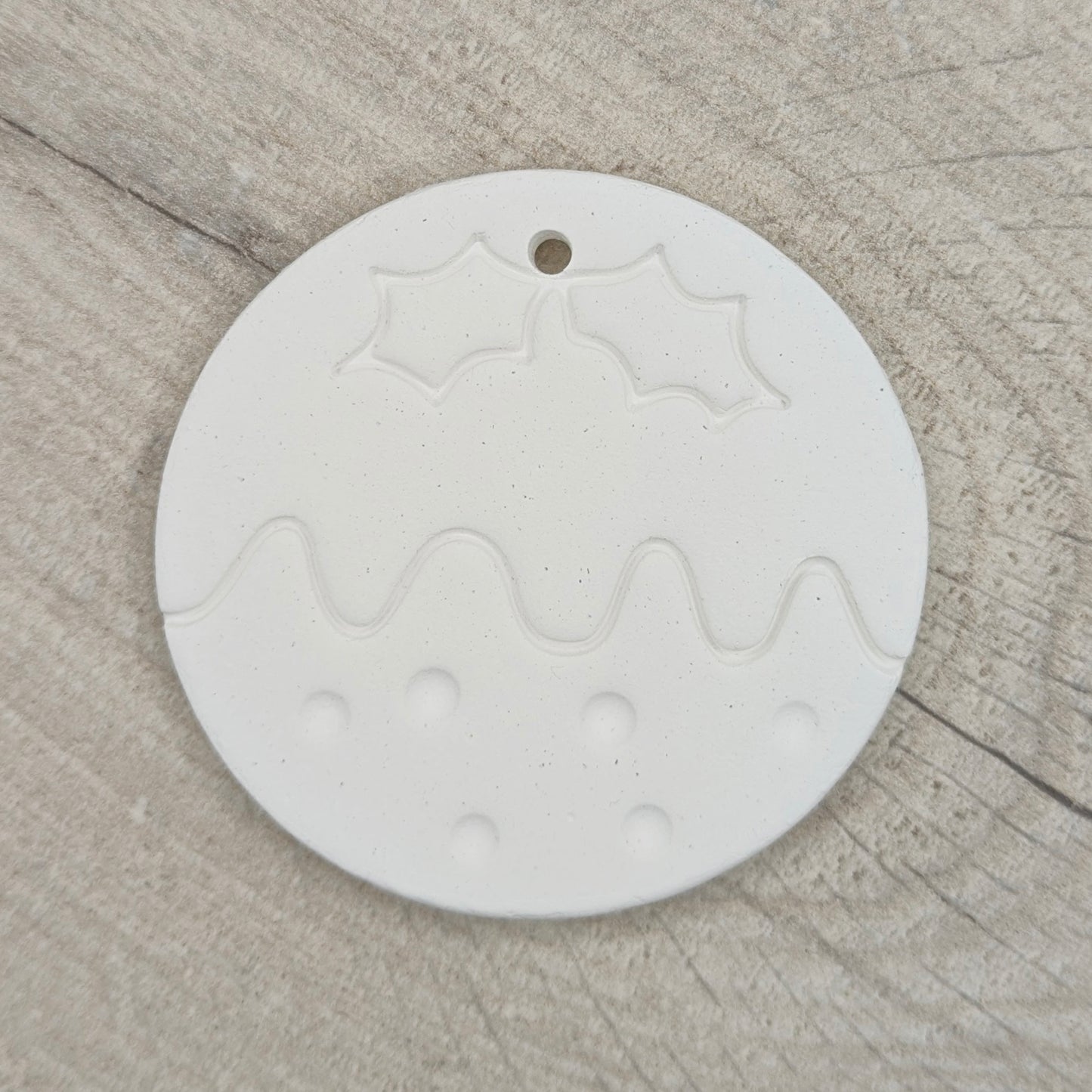 round christmas pudding shaped clay decoration to paint yourself on a wooden background