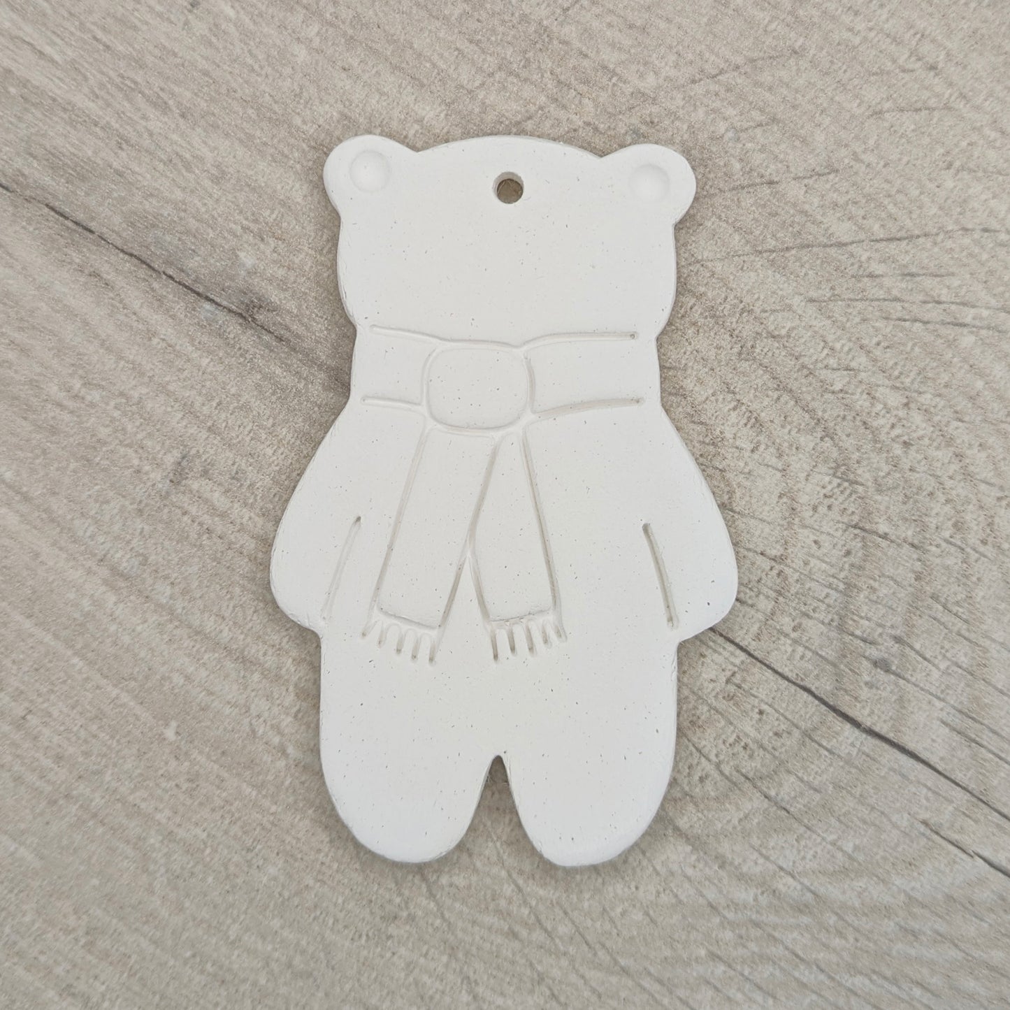 white air dried clay teddy bear ornament with a scarf stamped on, on a wooden surface