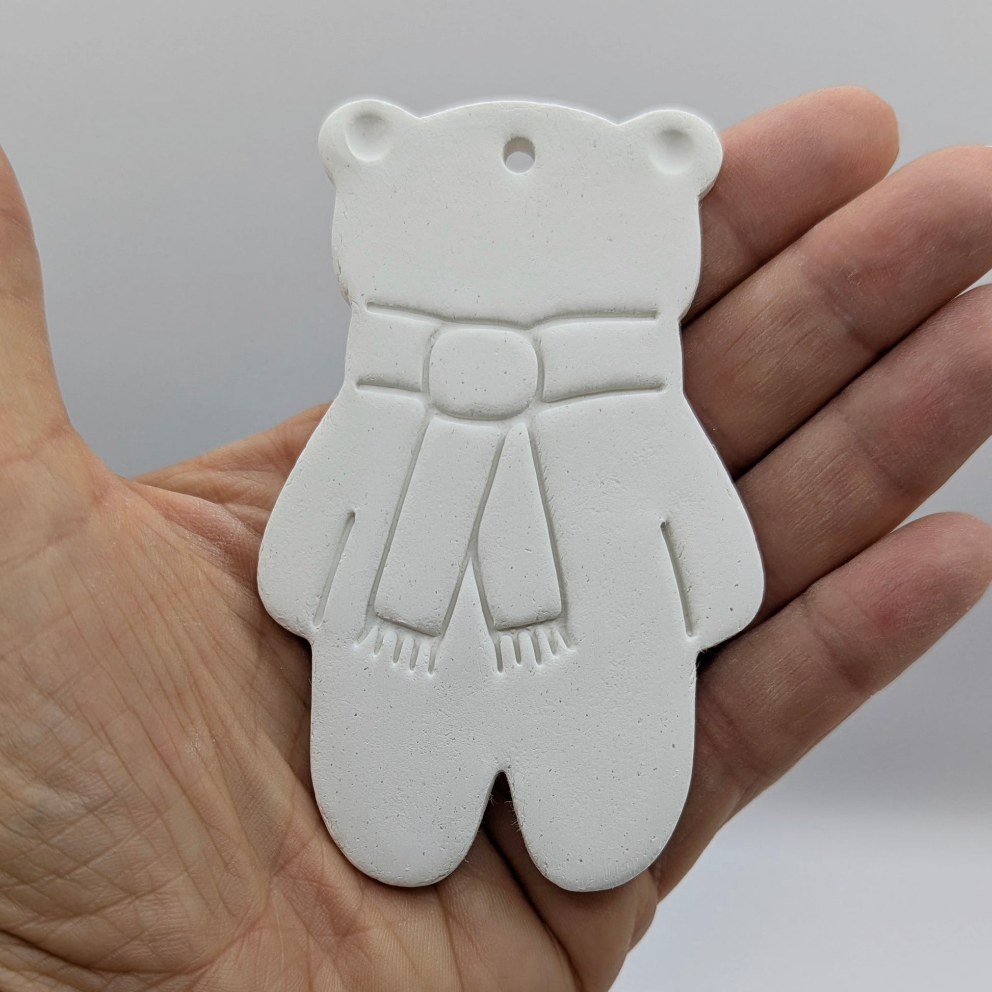 white air dried clay teddy bear ornament with a scarf stamped on, held in some ones hand