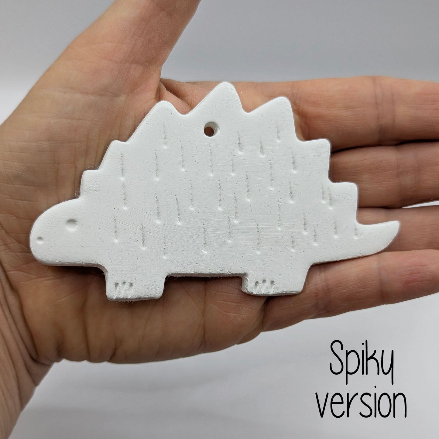spiky Stegosaurus dinosaur air dried clay decoration held in a hand for scale