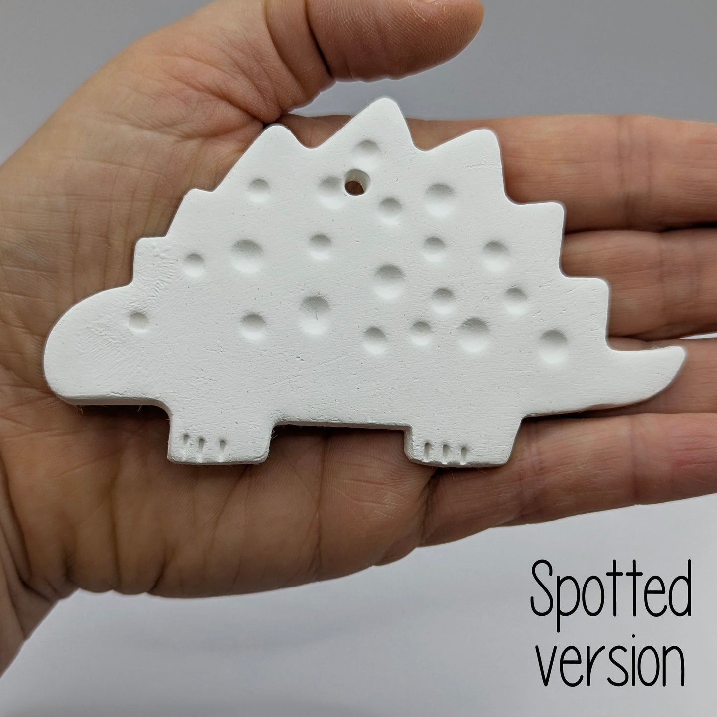 spotted Stegosaurus dinosaur air dried clay decoration held in a hand for scale