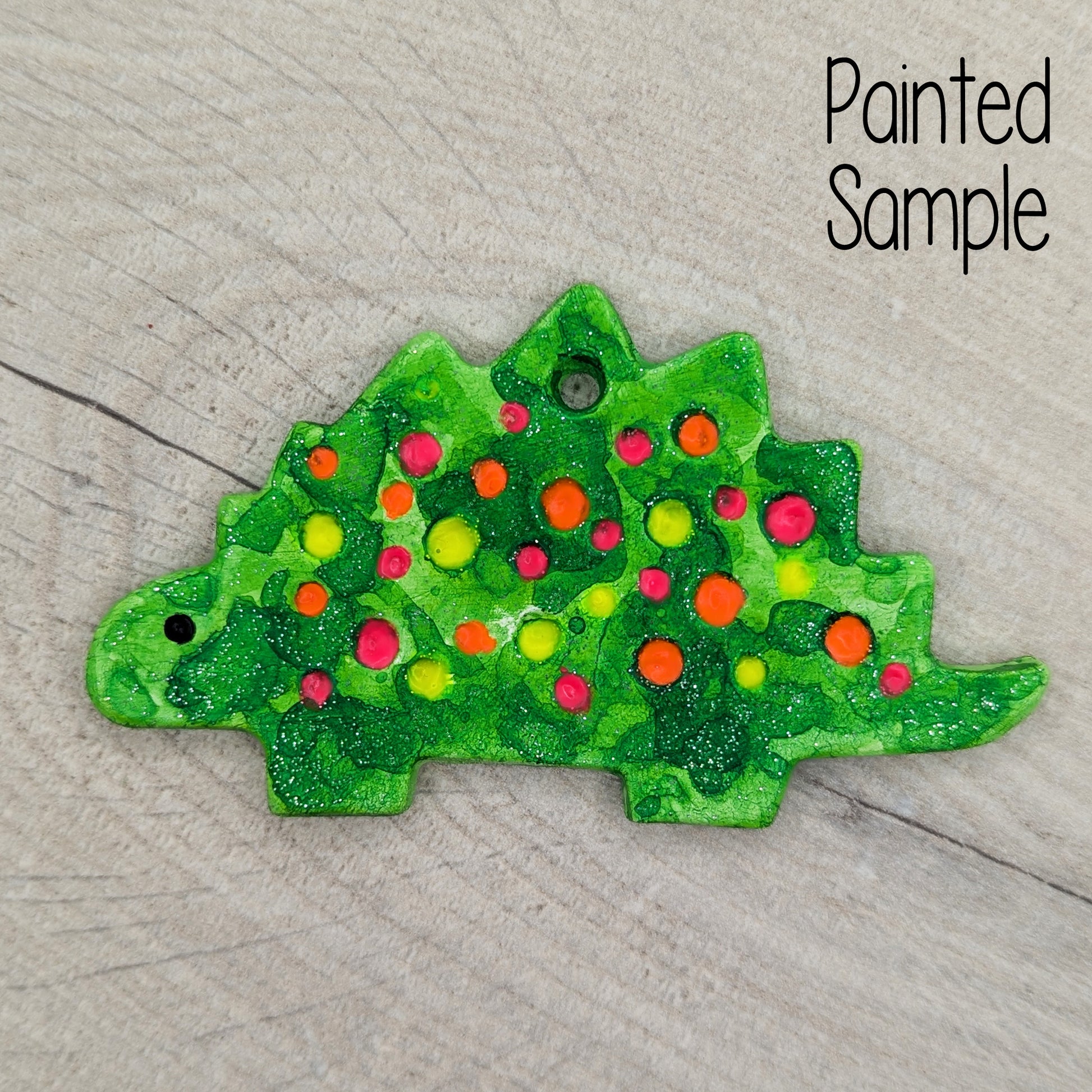 glittery green painted Stegosaurus dinosaur clay decoration with neon yellow, pink and orange spots 