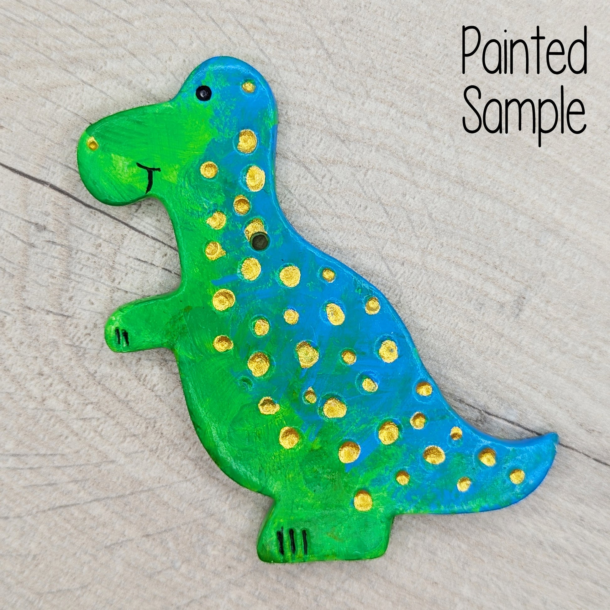 green and blue painted Tyrannosaurus dinosaur clay decoration with gold spots and black sharpie details