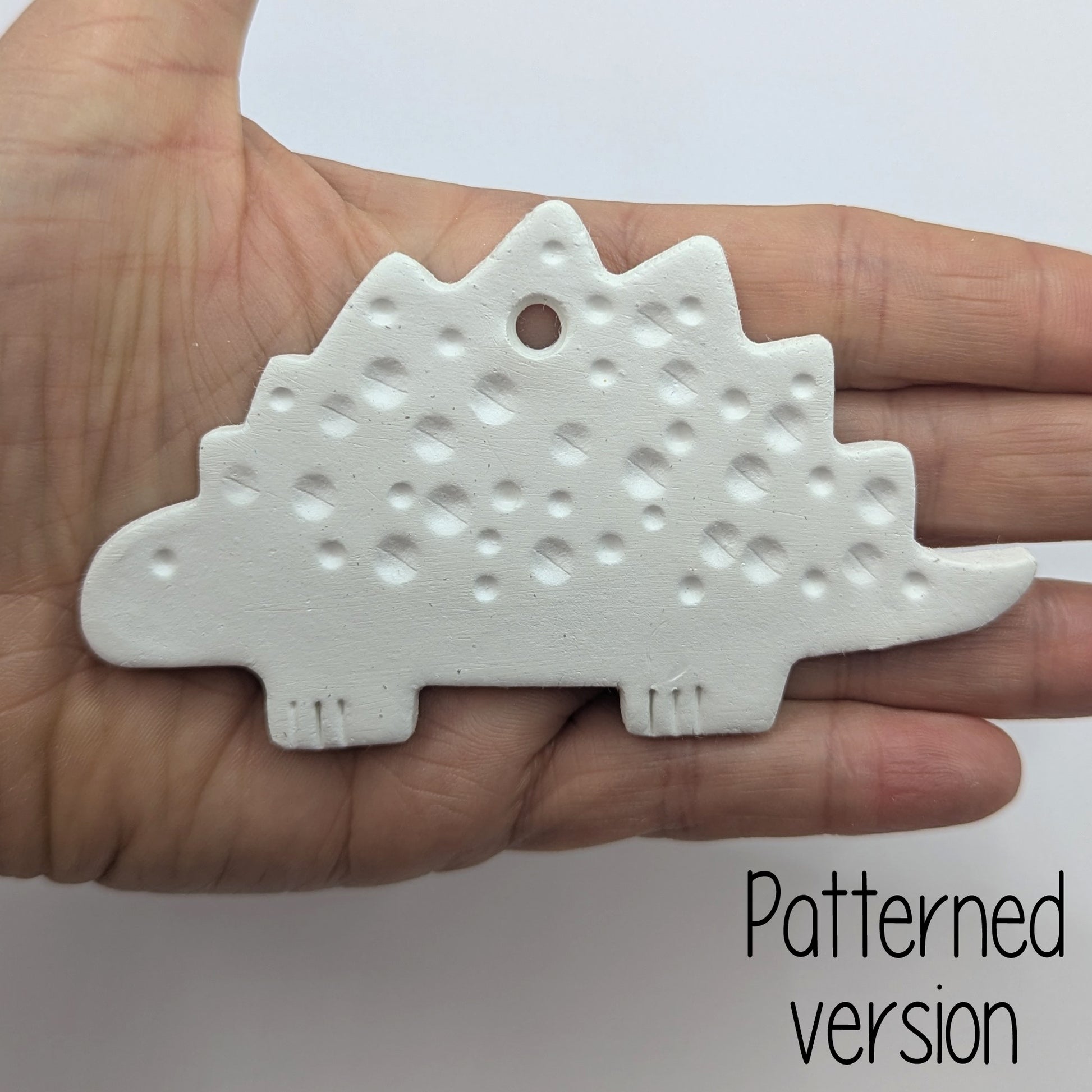 spotted Stegosaurus dinosaur clay decoration, shown in ladies hand for scale