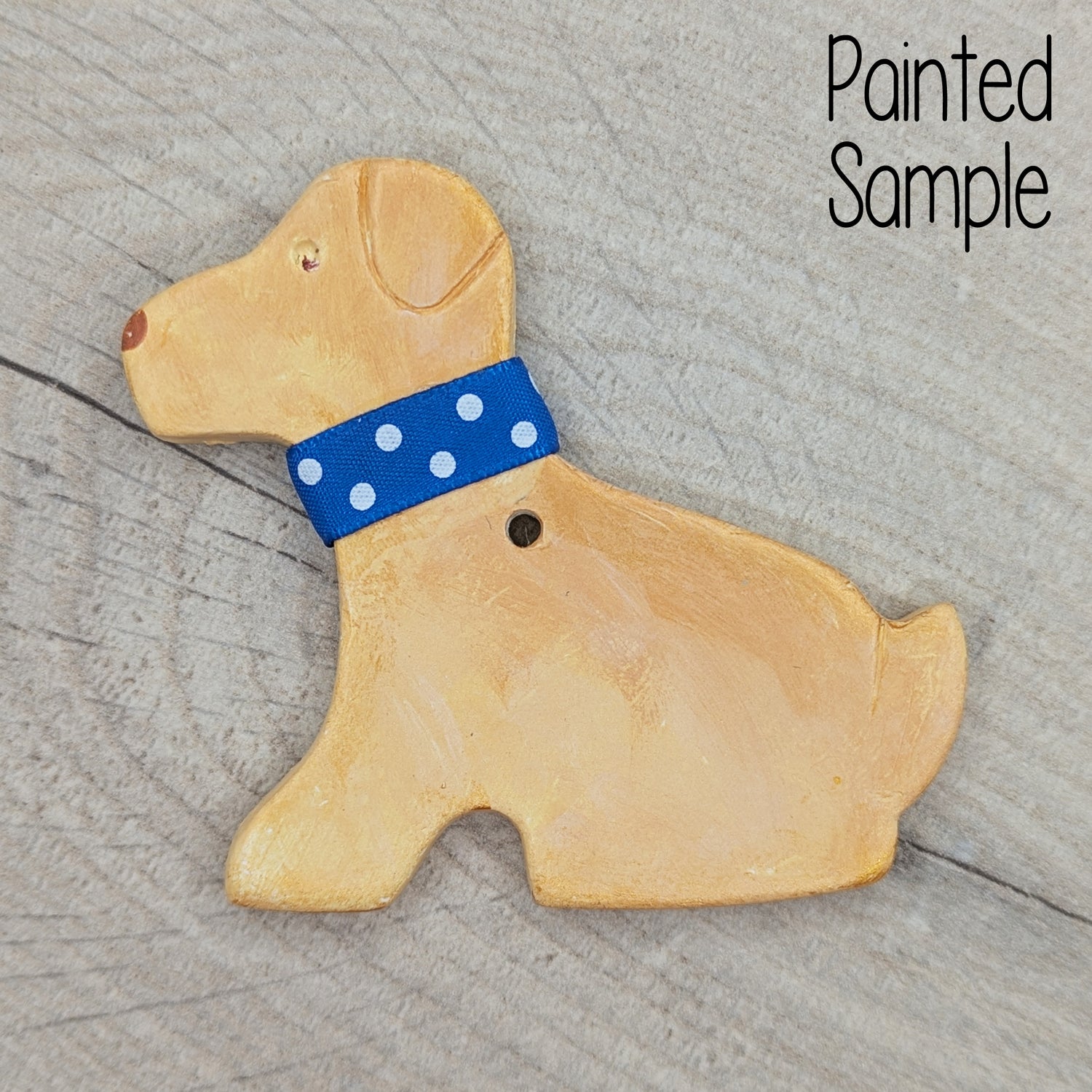 clay decoration of a Labrador painted to look like a golden labrador with a blue with white spotted ribbon collar
