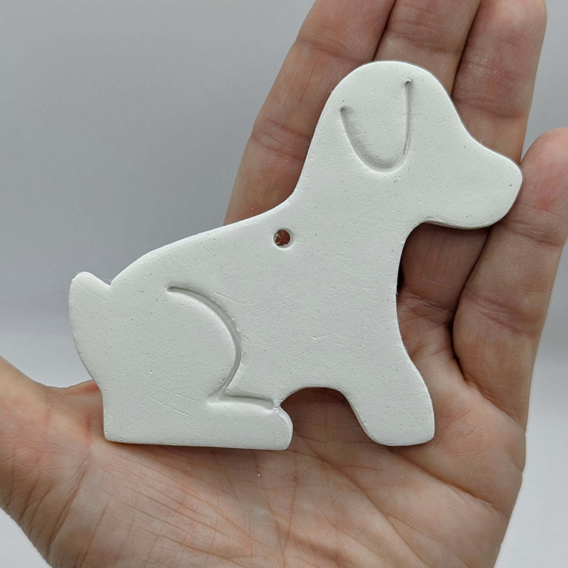White air dried clay dog-shaped ornament held in a hand against a neutral background