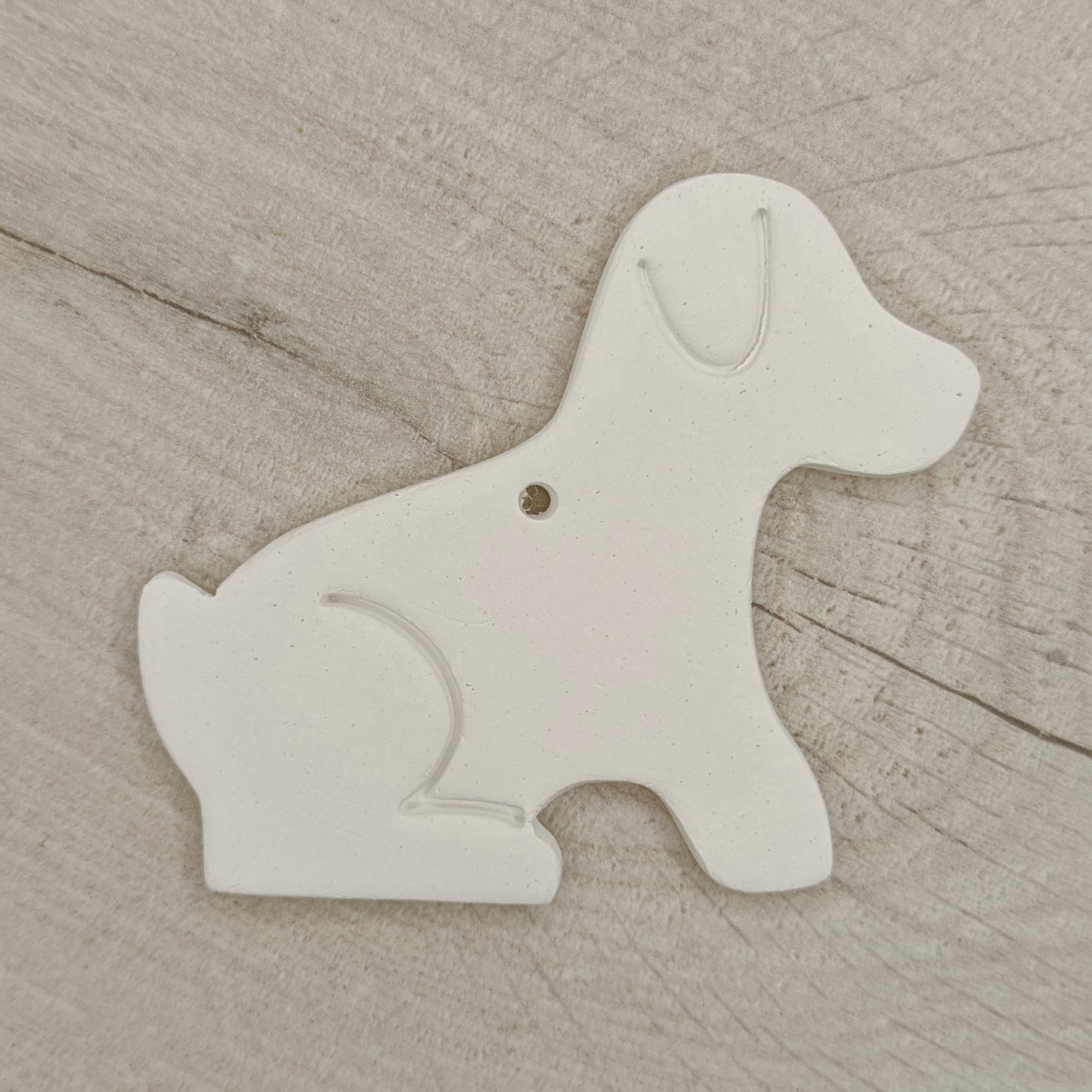 White air dried clay dog-shaped ornament on a wooden background