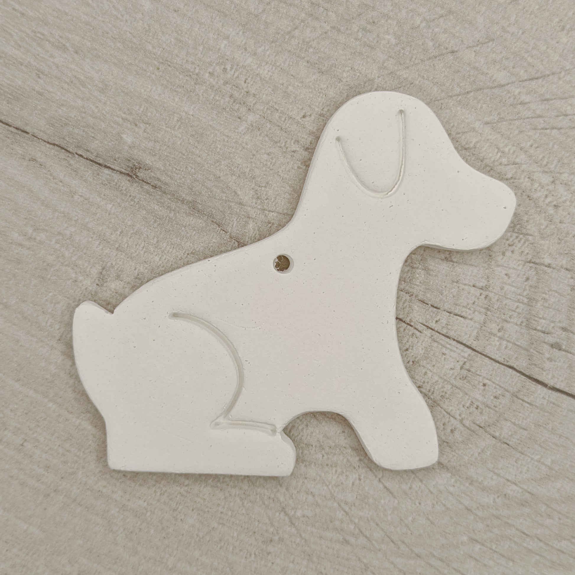 White air dried clay dog-shaped ornament on a wooden background