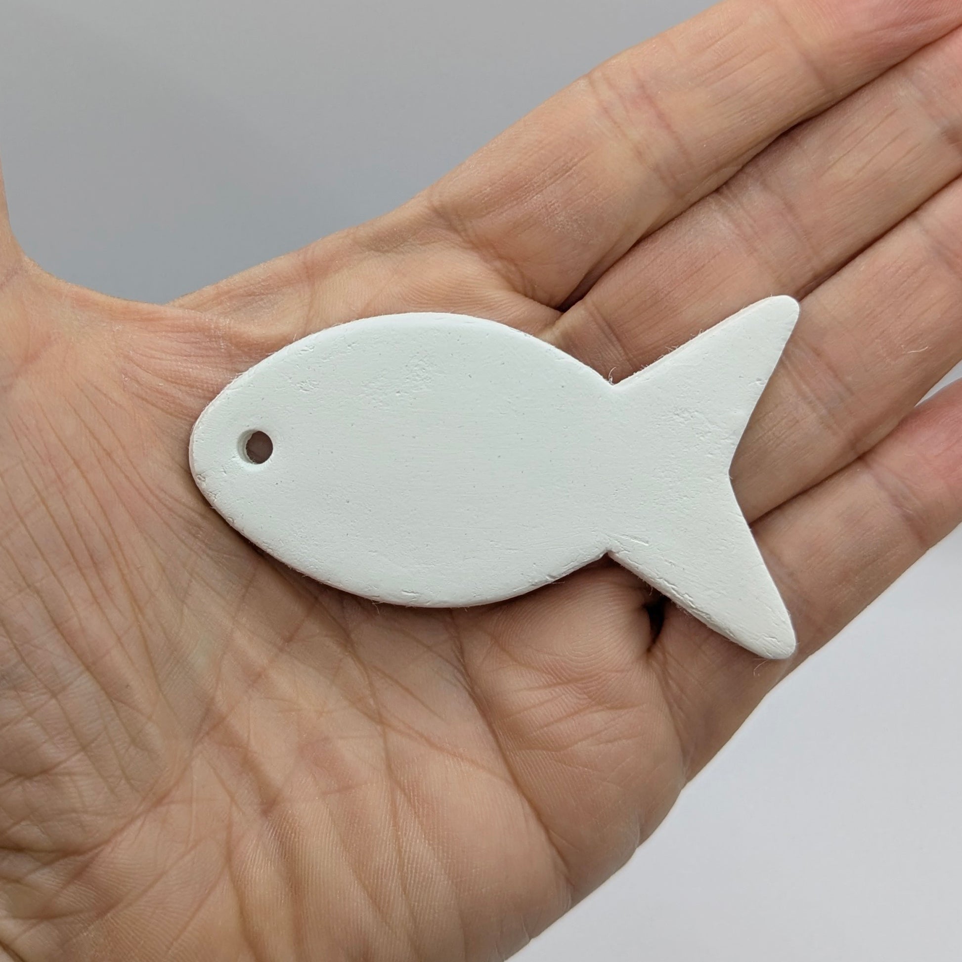White fish-shapeddecoration held in a hand against a neutral background